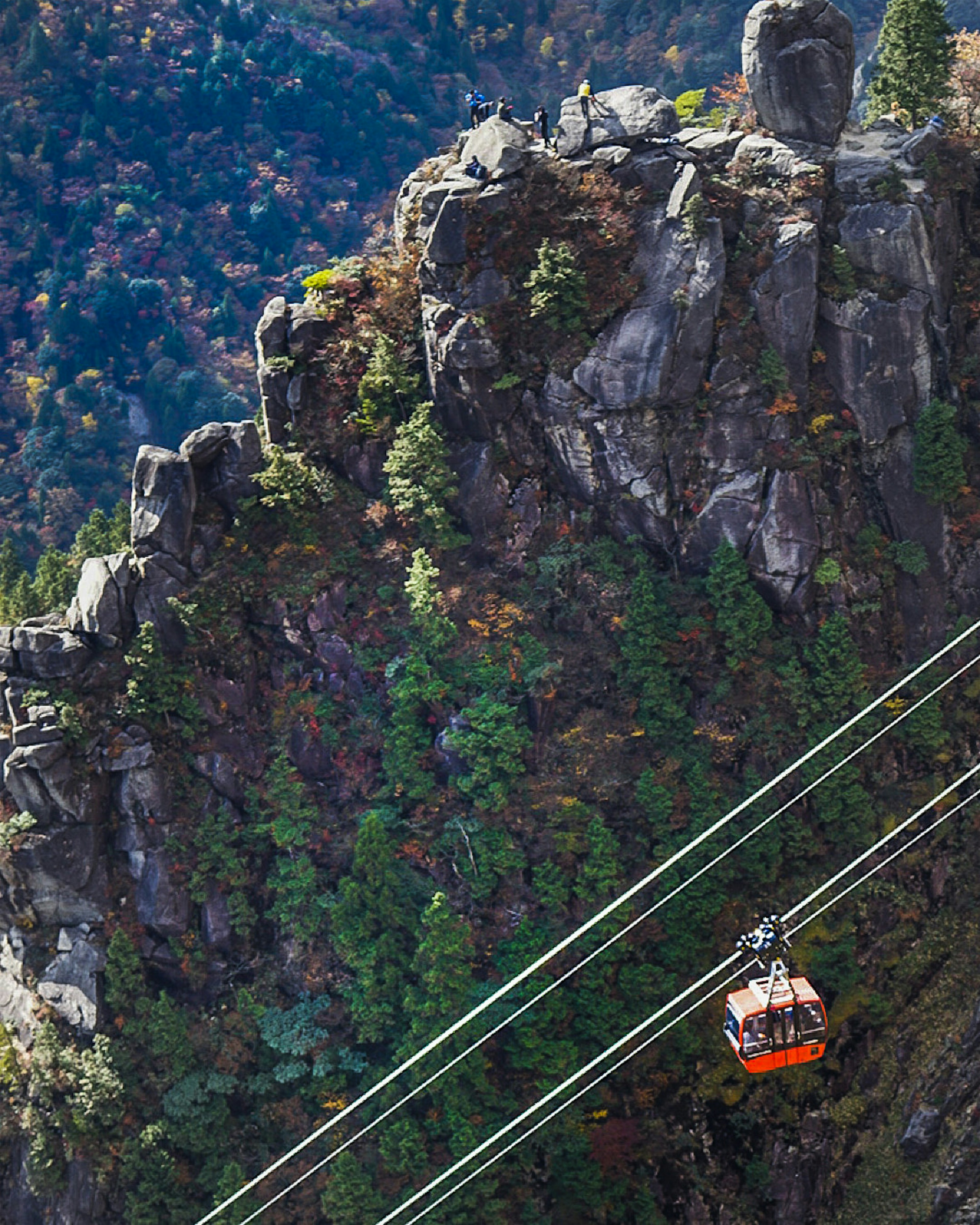 A cable car traveling over rocky terrain with colorful trees in the background