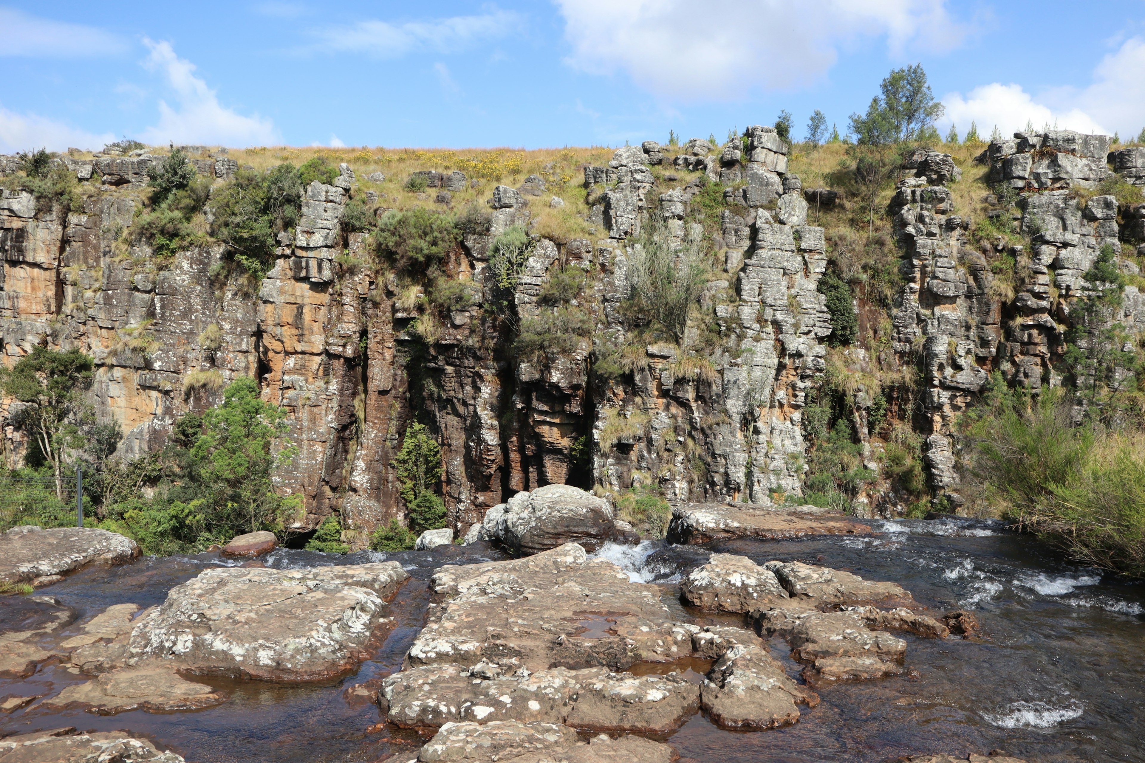 Immagine di scogliere rocciose accanto a un fiume con vegetazione e cielo blu