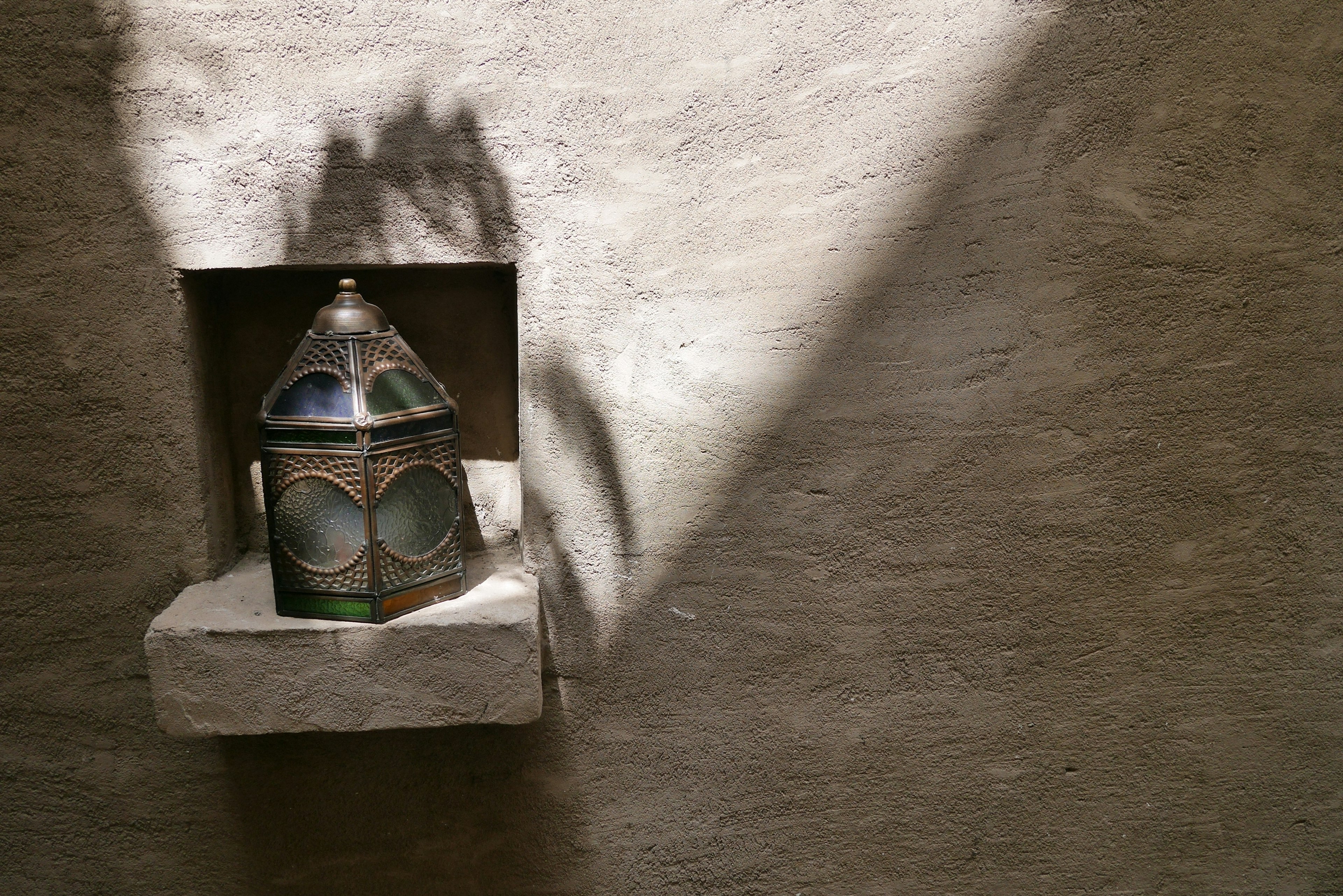 A beautifully designed lantern placed in a wall niche with sunlight casting shadows