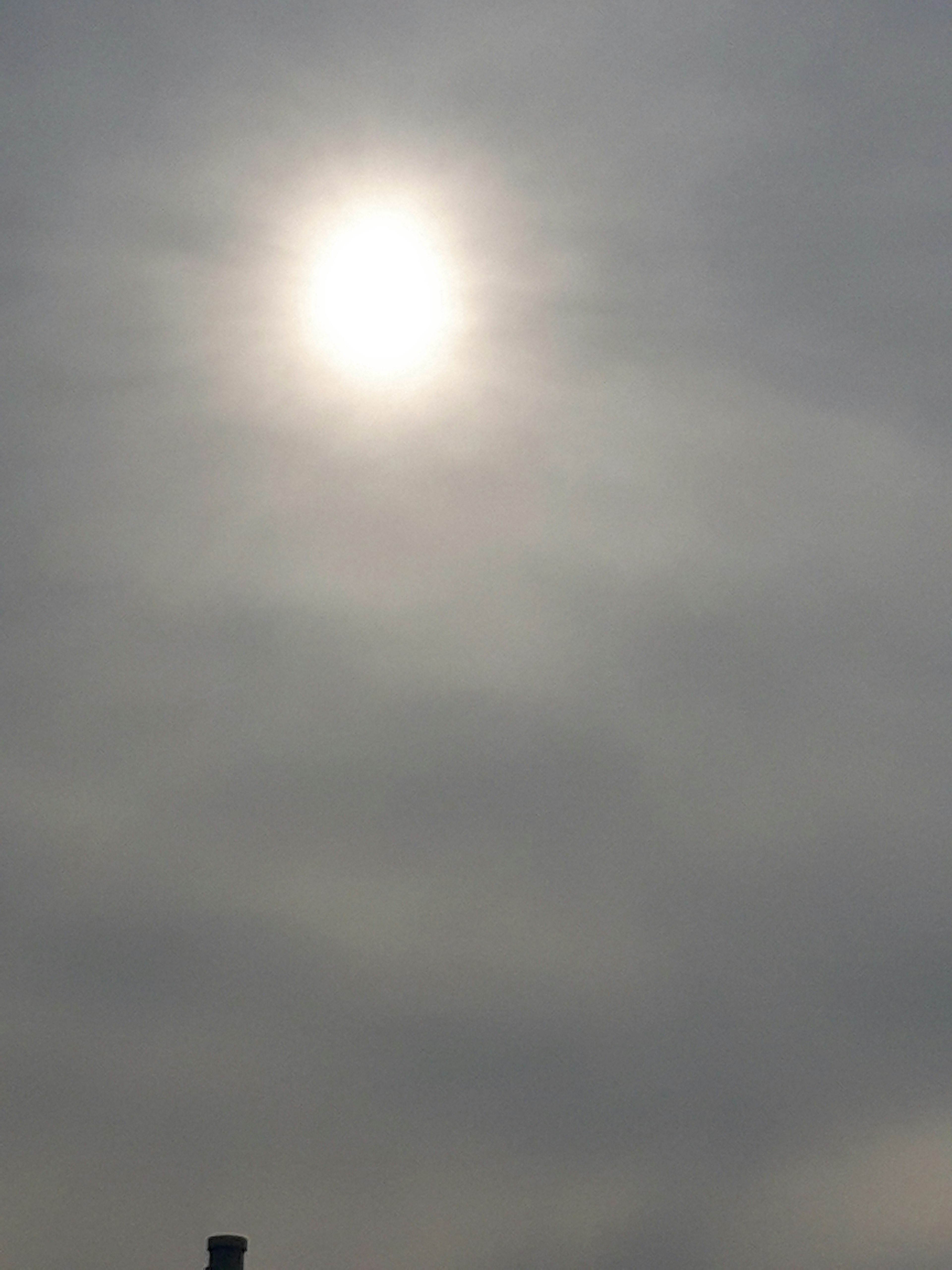 Sonne von dünnen Wolken in einem grauen Himmel verdeckt