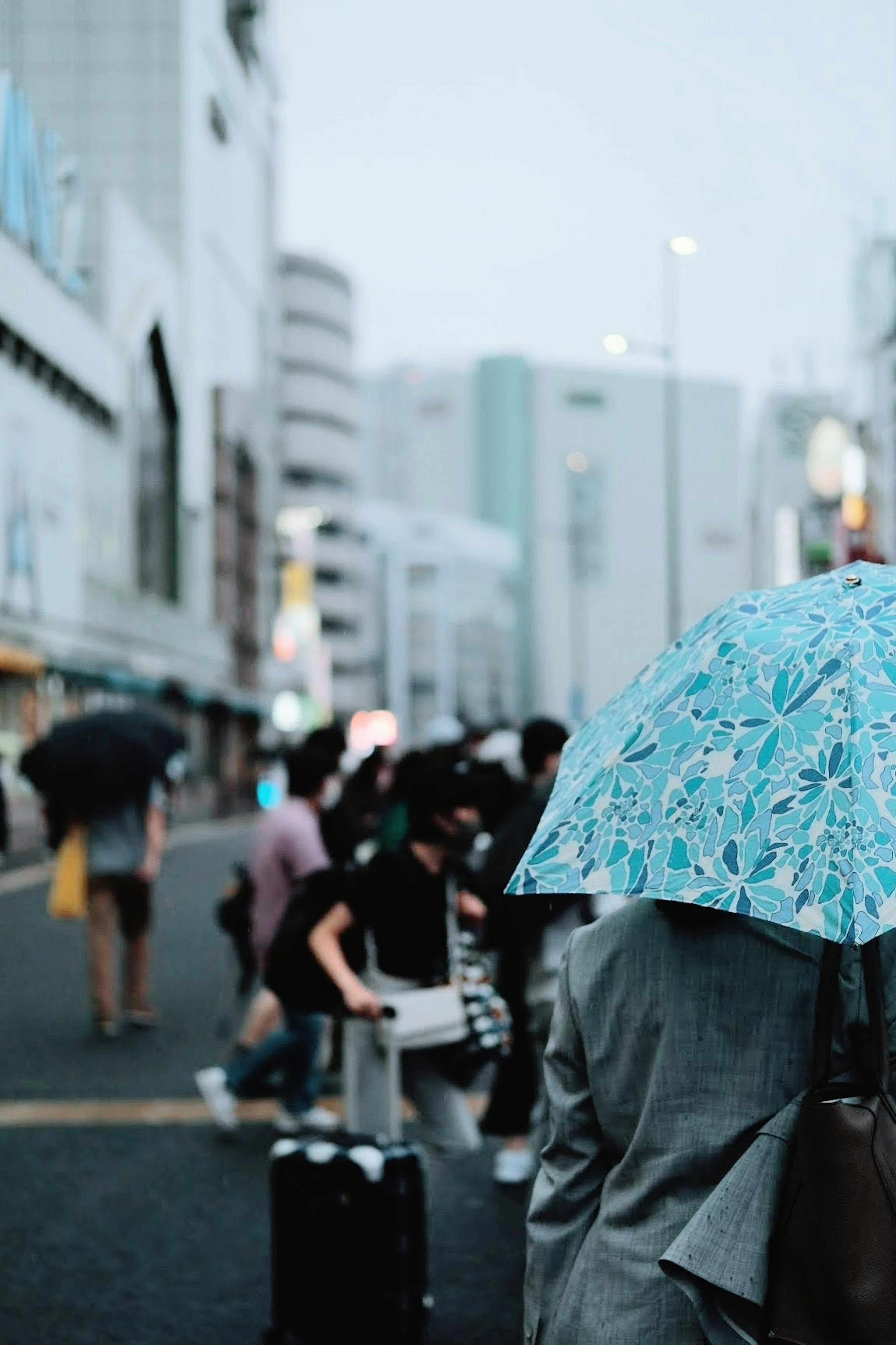 青い傘を持った人々が行き交う都市の風景