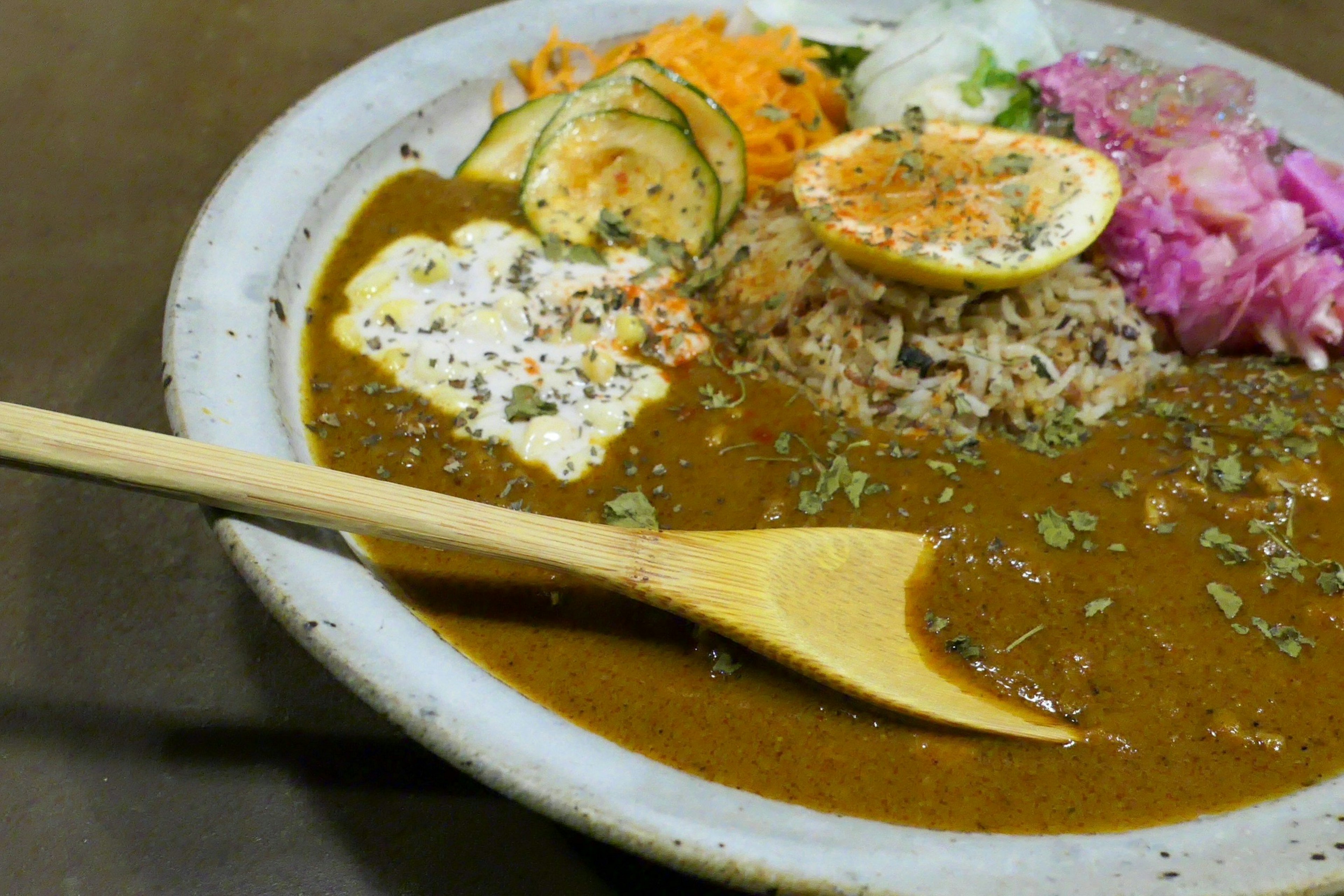 Curry rice served with fresh vegetable toppings and a wooden spoon