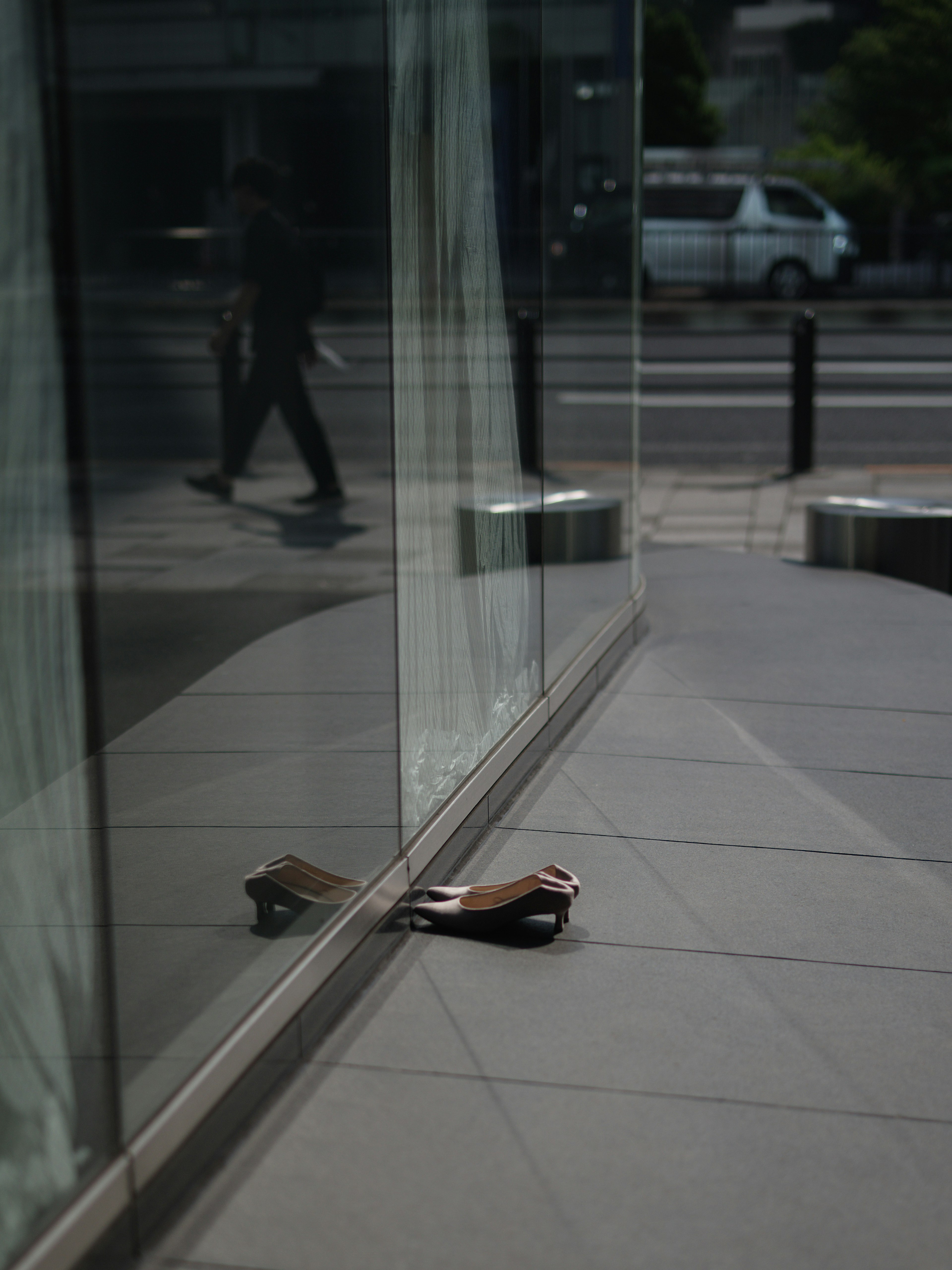 Un zapato marrón dejado en la acera con su reflejo en una ventana de vidrio