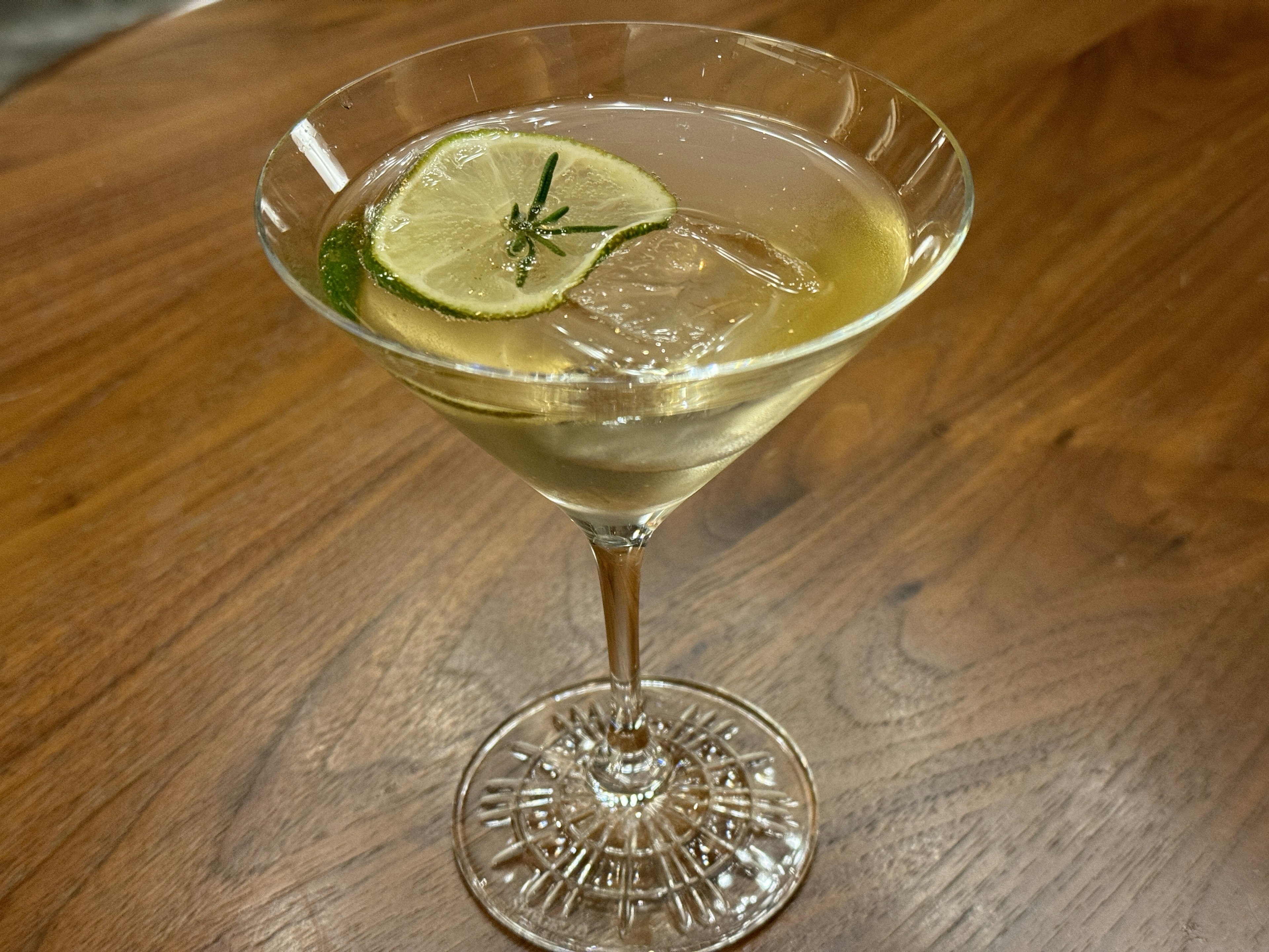 Un verre à cocktail avec une boisson garnie d'une tranche de lime et d'herbes