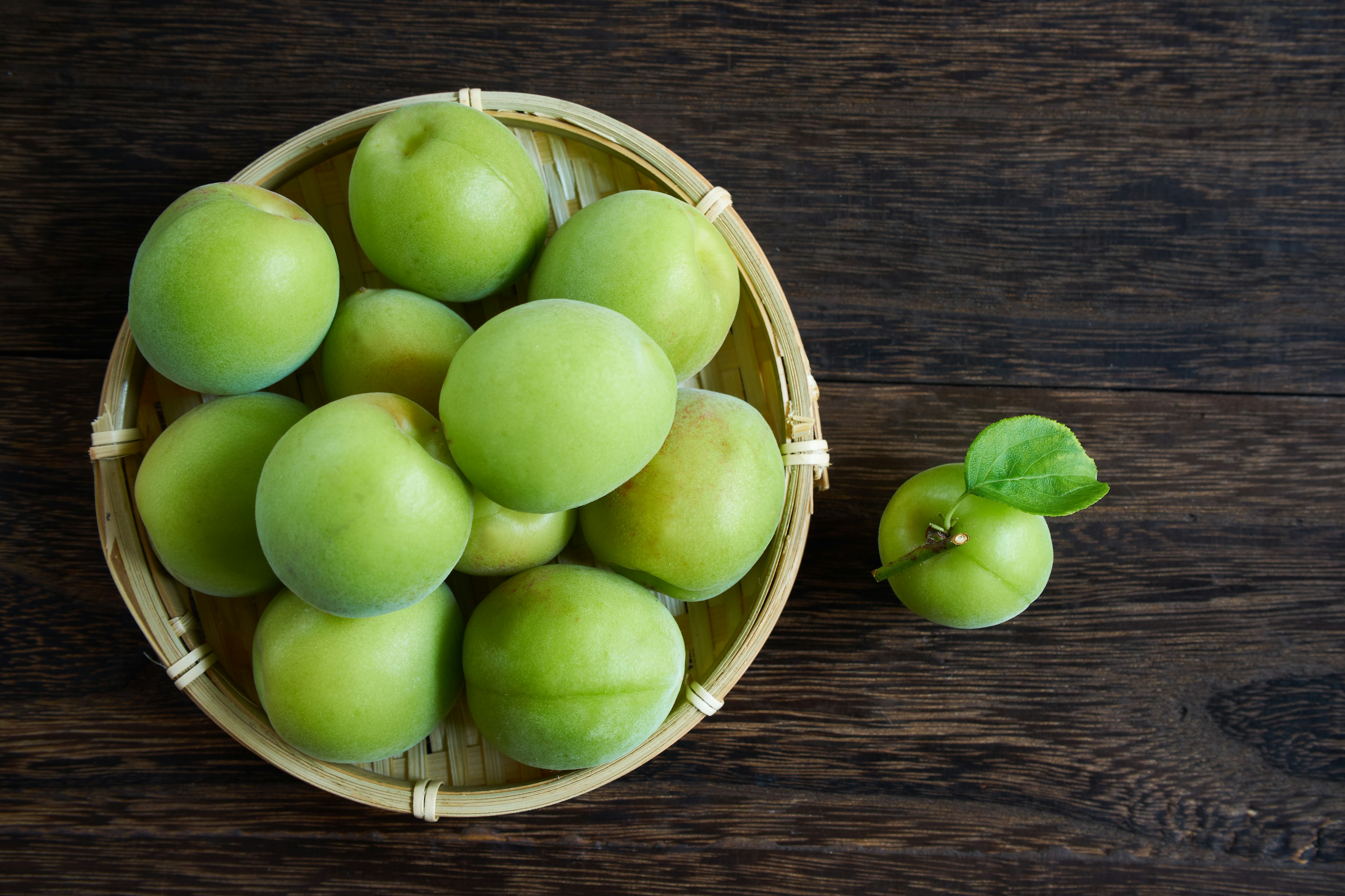 Plum hijau dalam keranjang anyaman dengan satu plum kecil di sampingnya