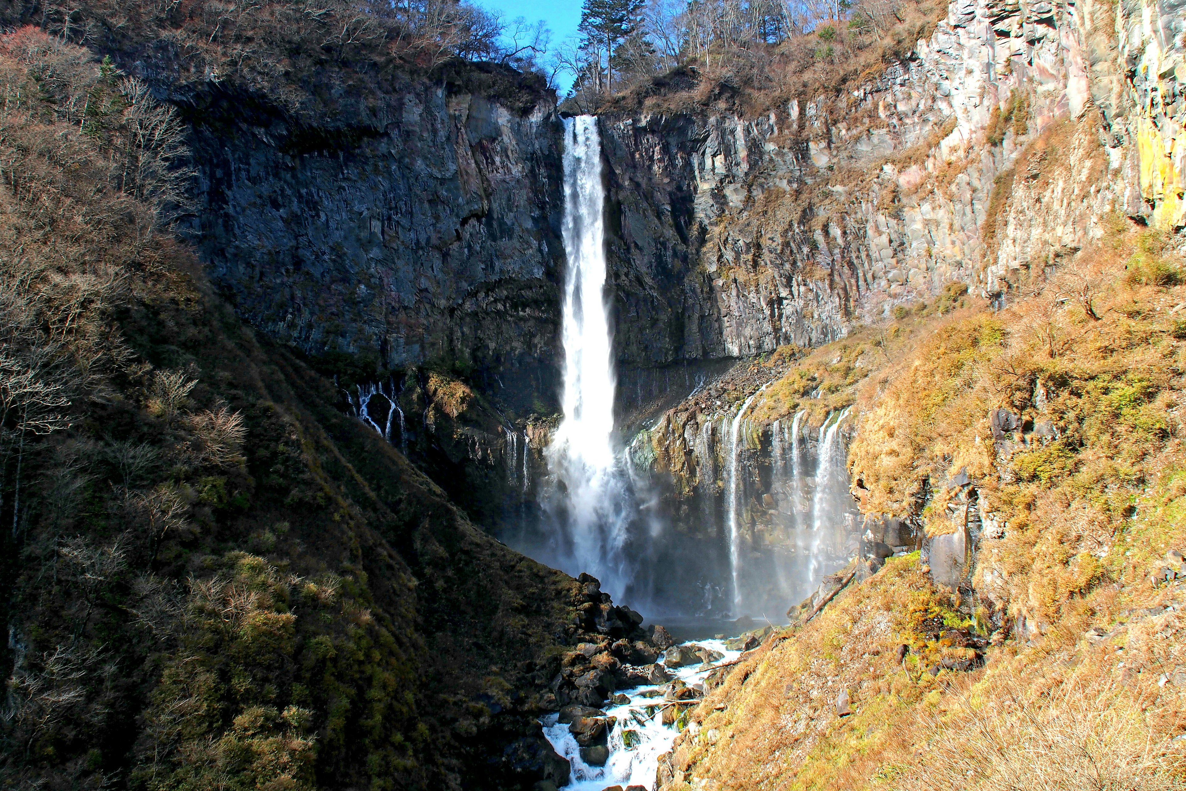 Ein atemberaubender Wasserfall, der von einer Felswand umgeben von herbstlichem Laub herabstürzt