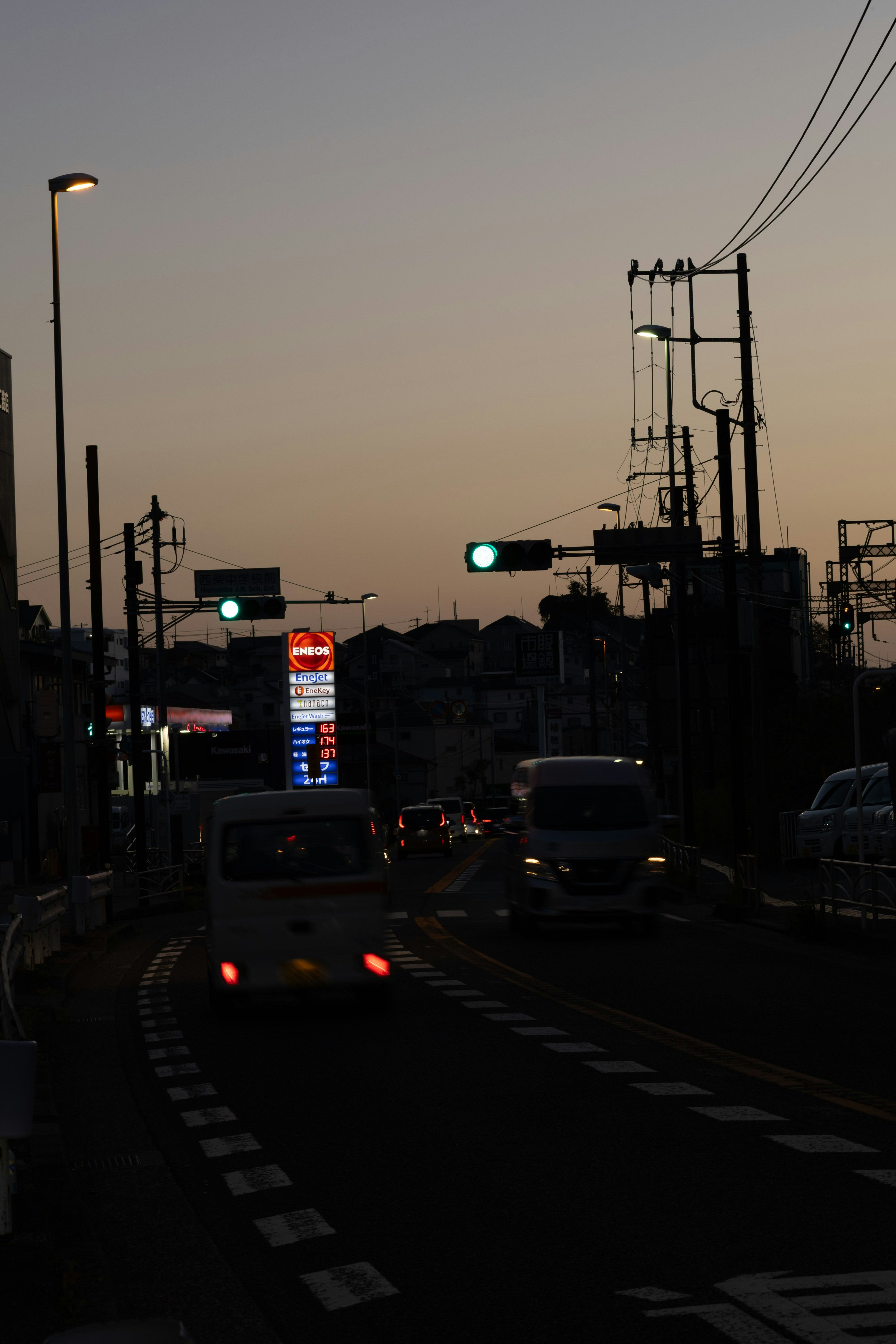 夕暮れ時の街並み 車両が走る道路 信号機と街灯が点灯