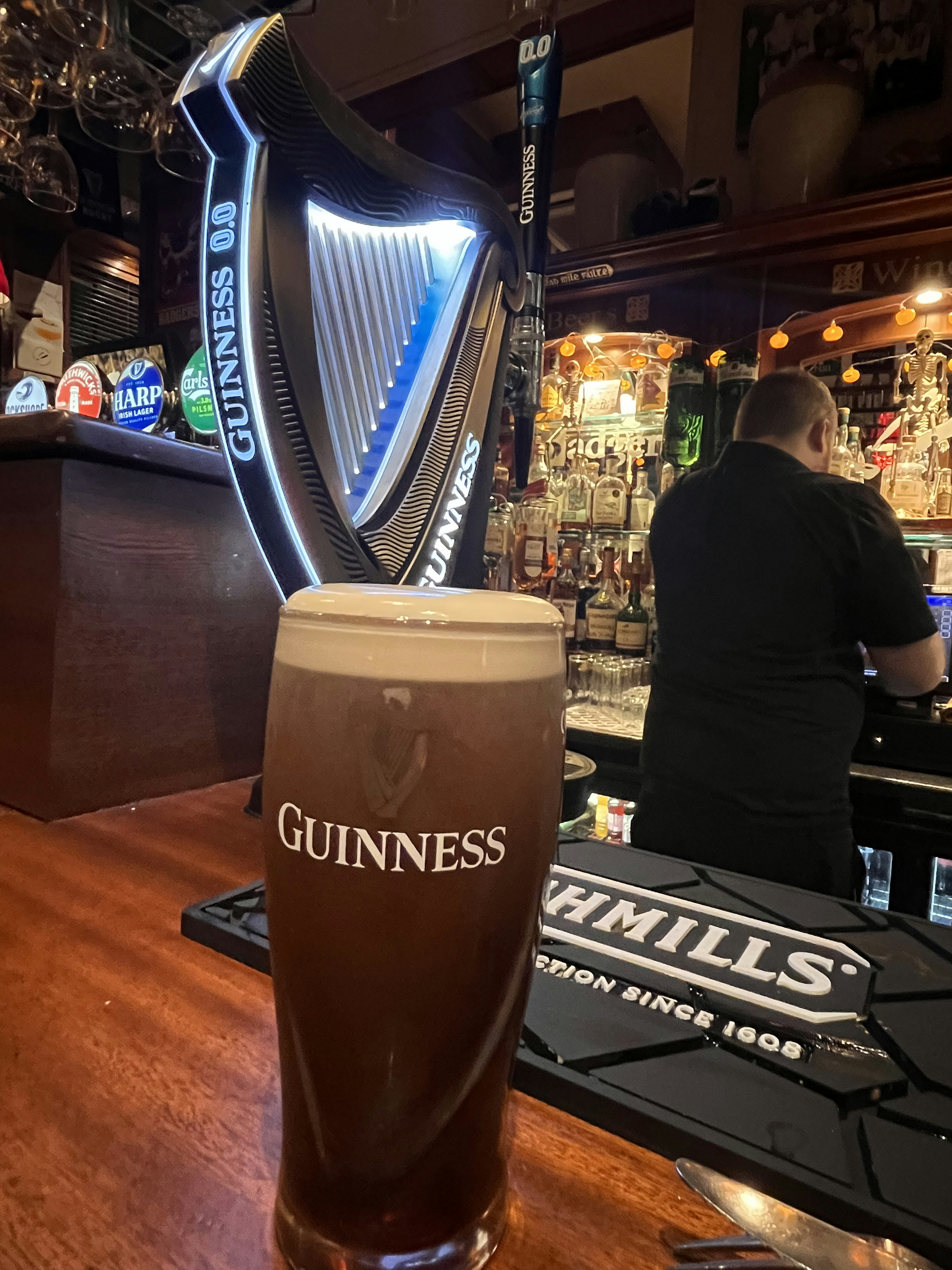 A glass of Guinness beer with a harp dispenser in a bar interior