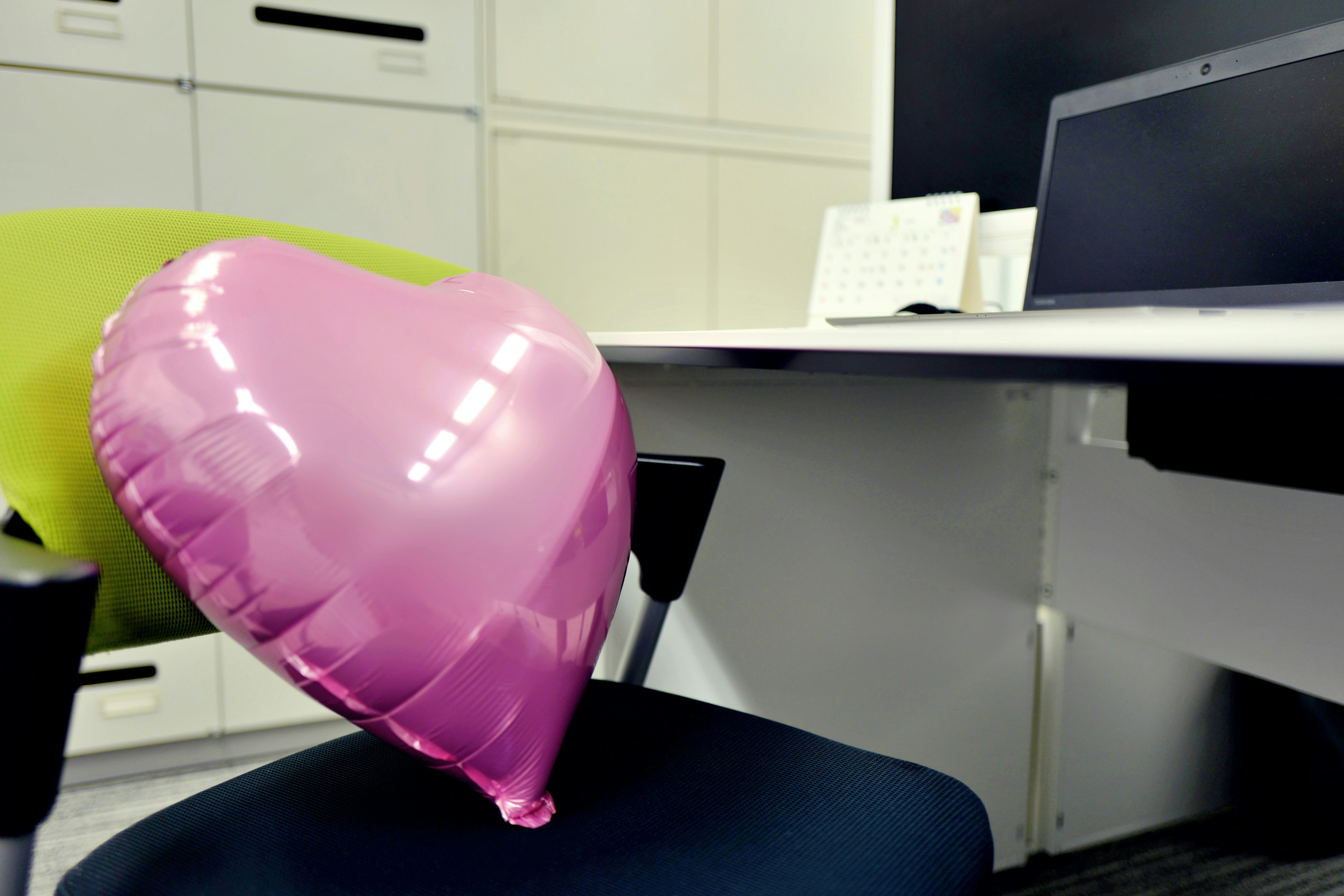 Balon berbentuk hati berwarna pink yang terletak di kursi dalam suasana kantor