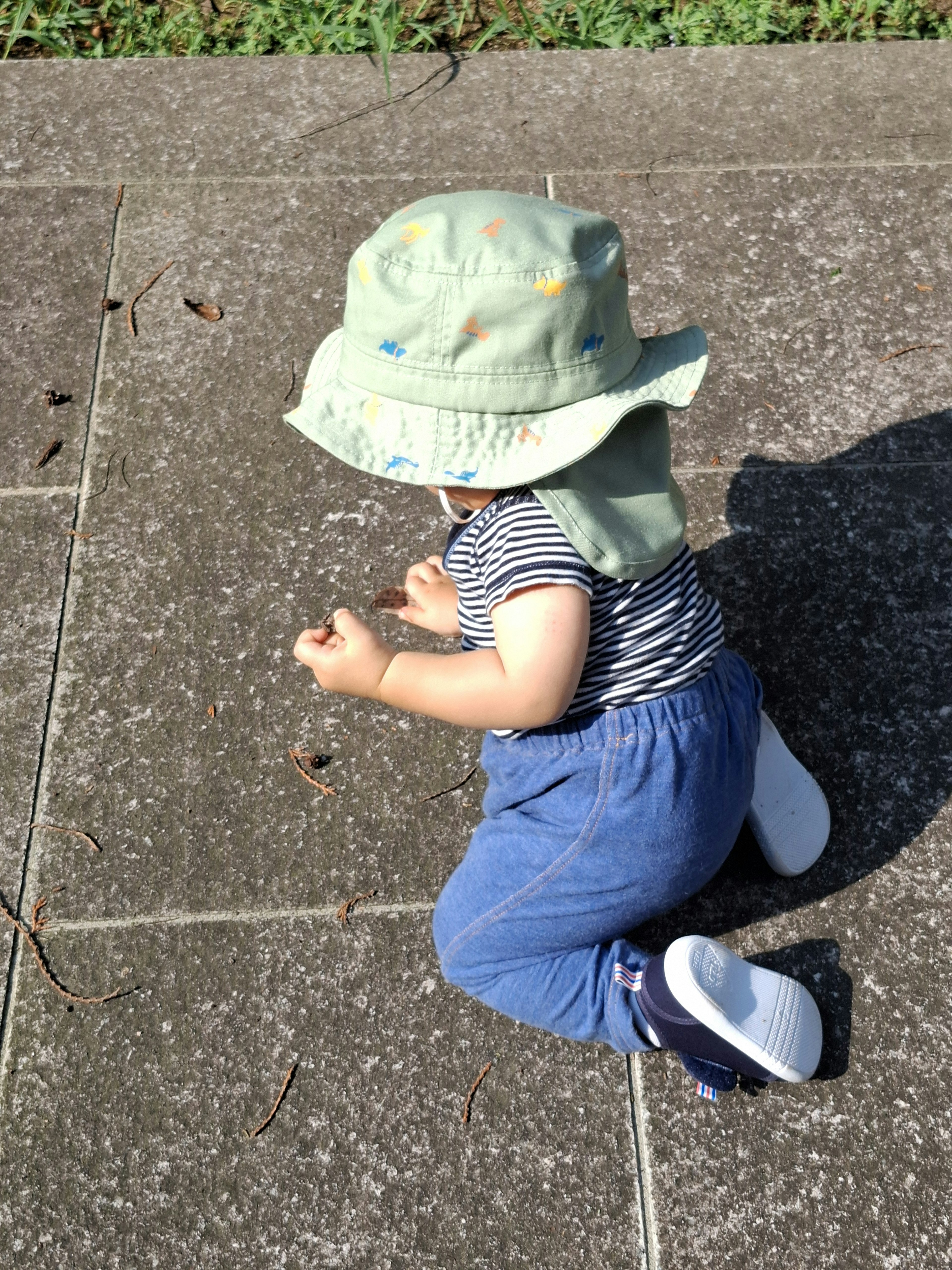 Baby in blue denim pants wearing a striped shirt and a green hat crawling on the ground