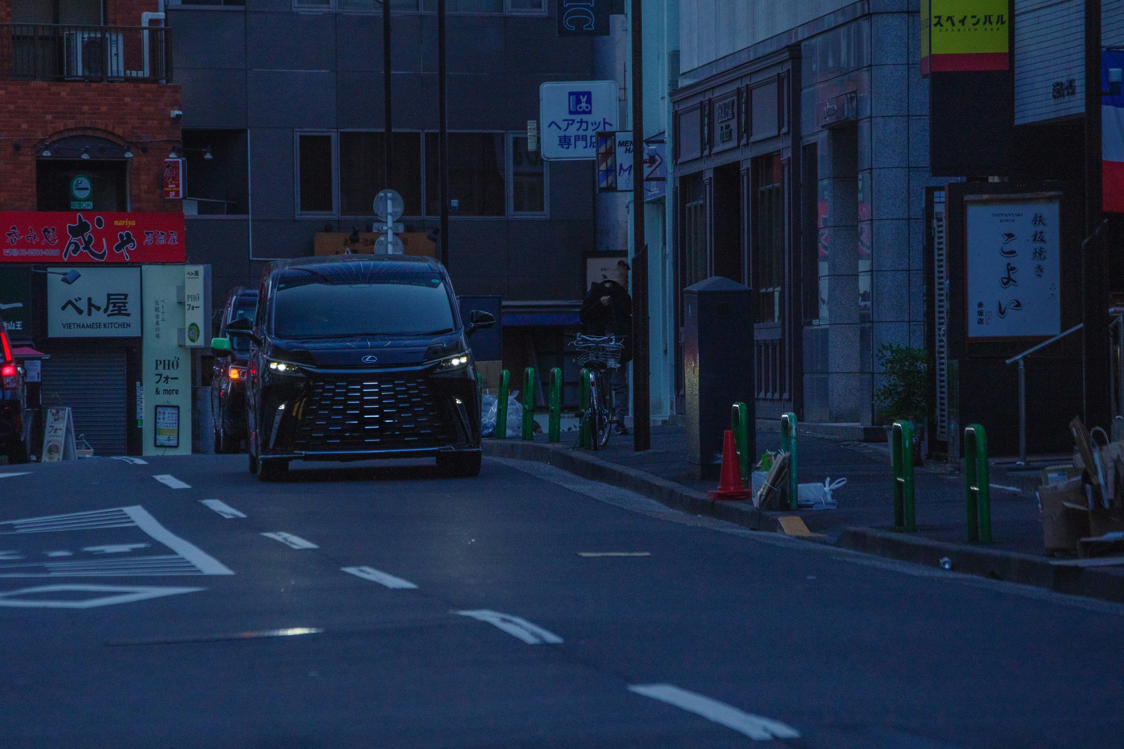 A black car driving down a dark street with urban surroundings
