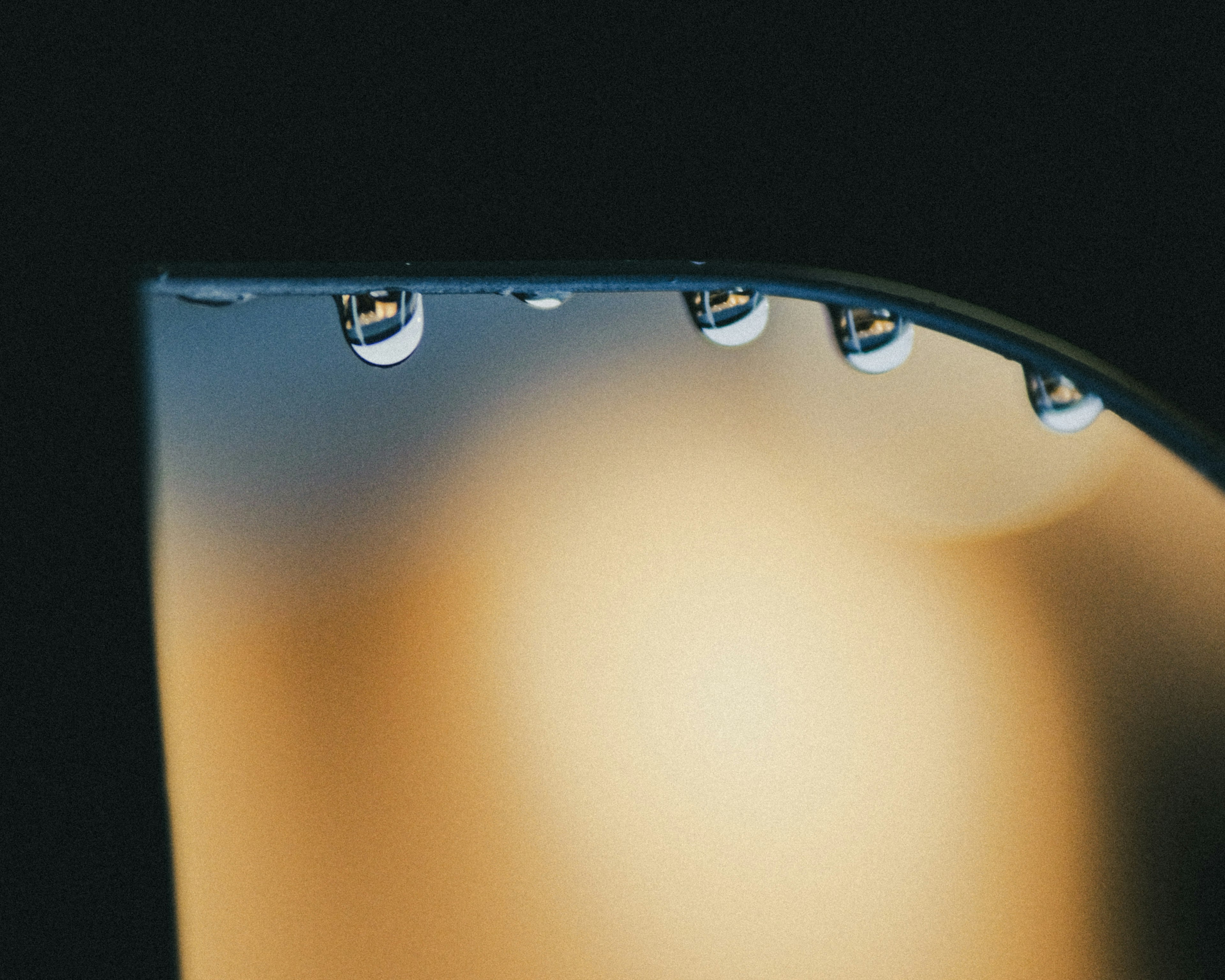 Close-up of water droplets on a curved edge of a lamp