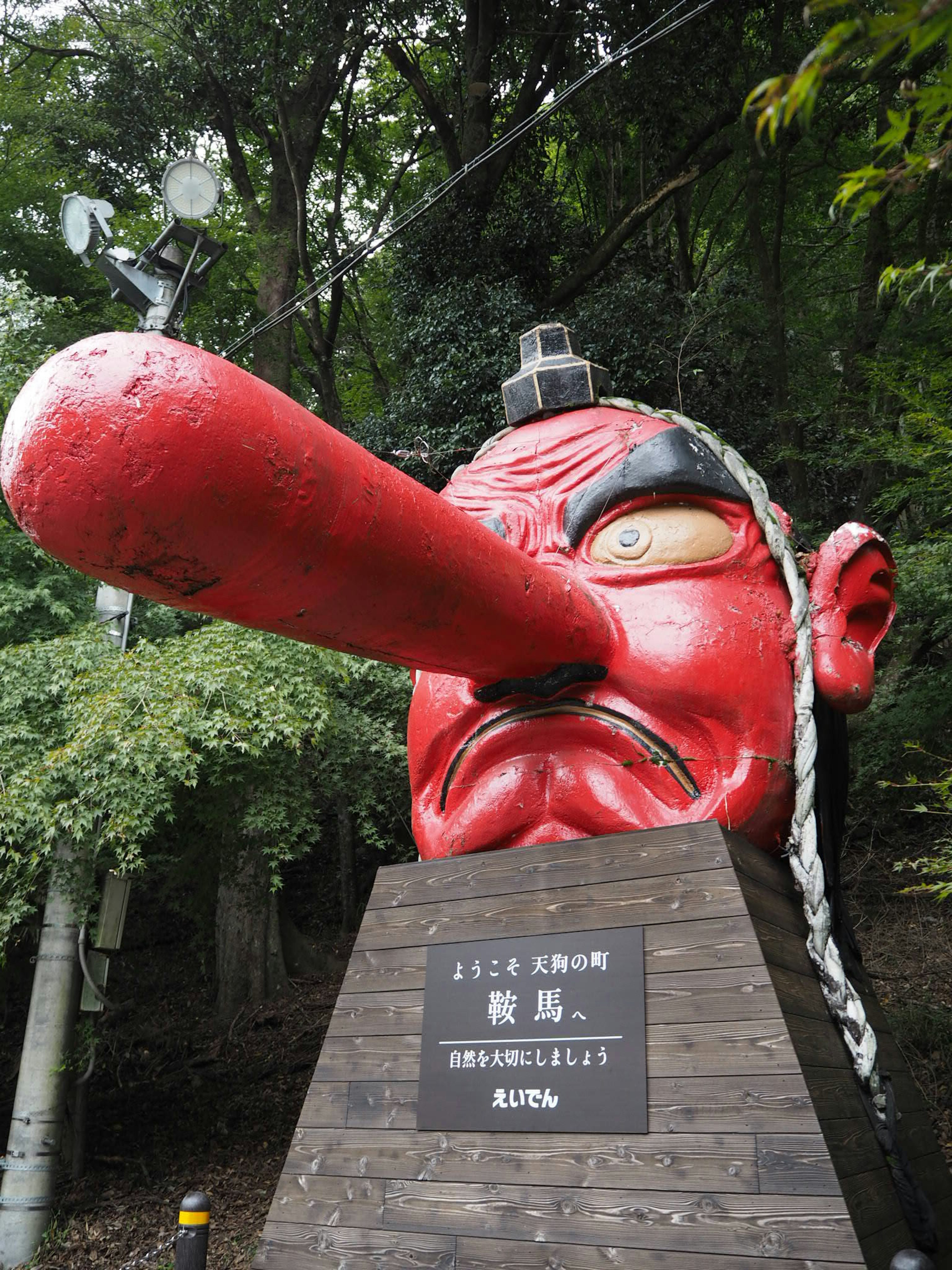 Grande statue avec un nez rouge située parmi des arbres verts