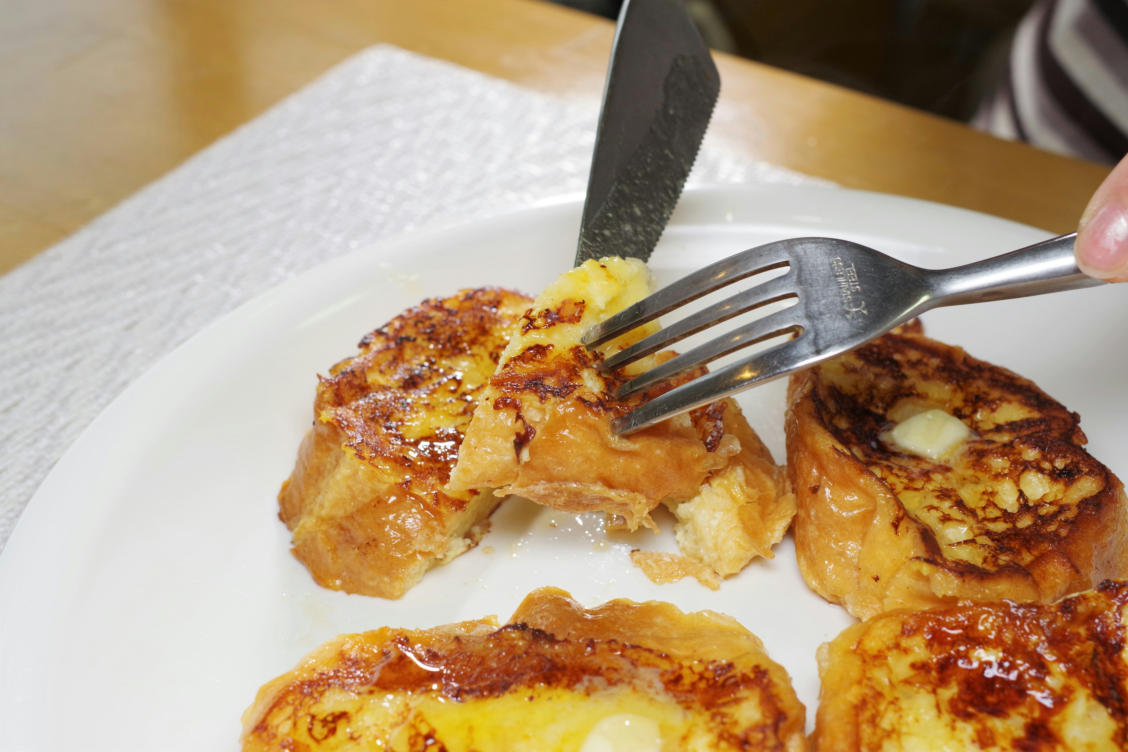 Primer plano de una rebanada de tostada francesa en un plato siendo cortada con un tenedor