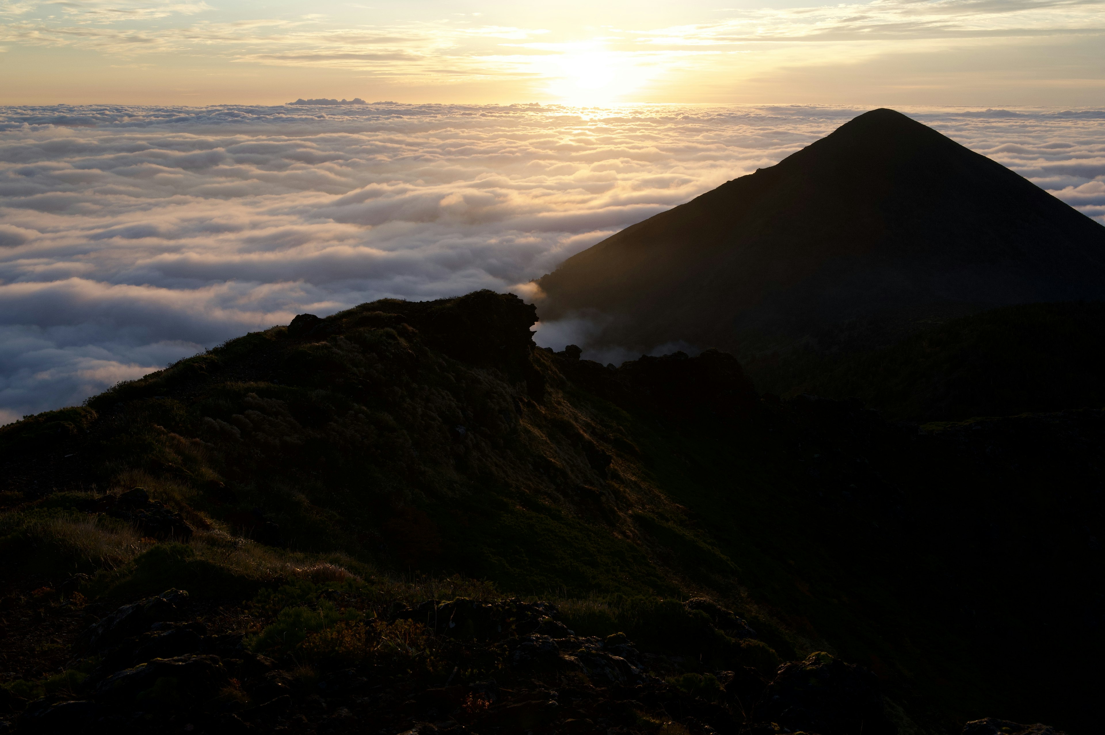 Silhouette di una montagna sopra un mare di nuvole al tramonto