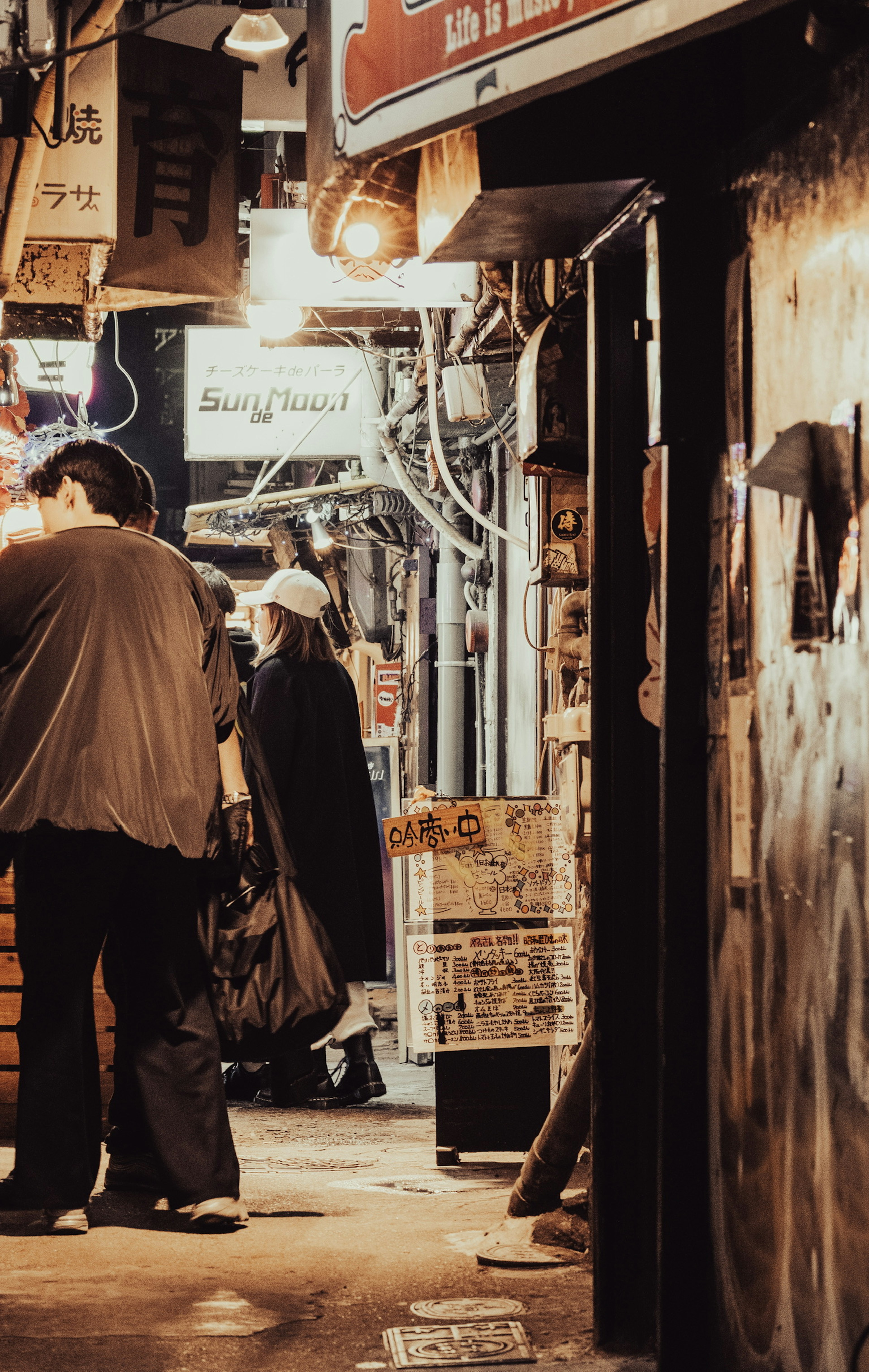 Des personnes se tenant dans une ruelle étroite la nuit des enseignes de magasins sont visibles