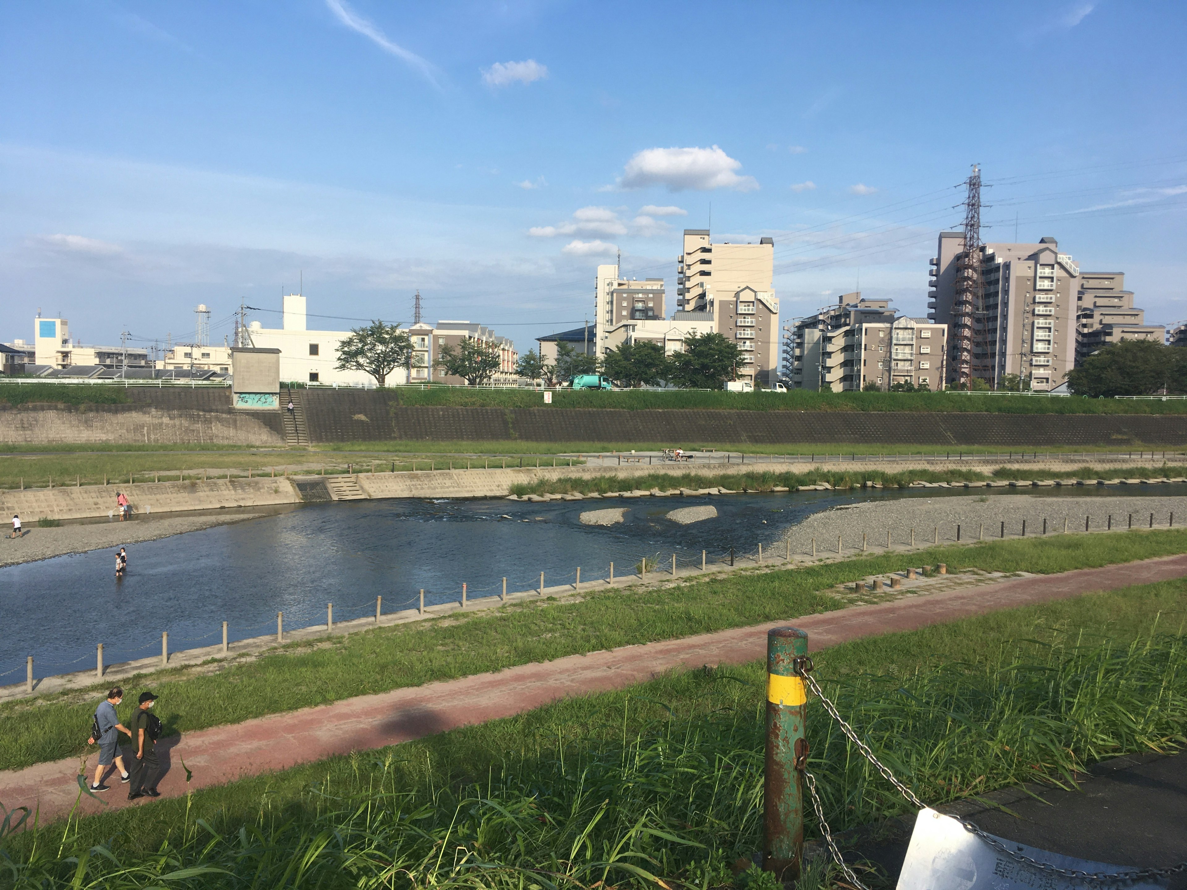 Riverside walkway with people walking alongside a river and city skyline