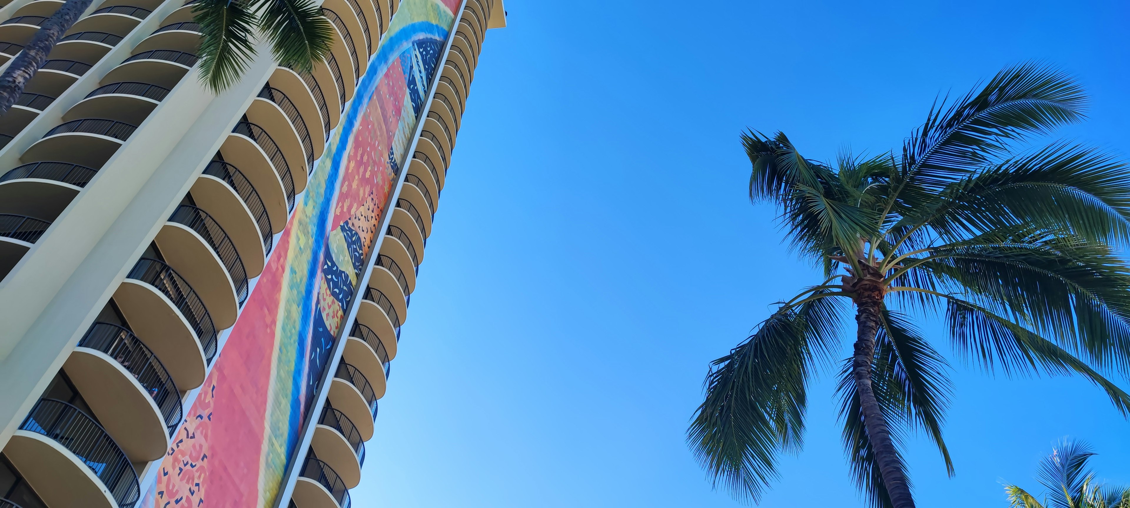 A tall building with a colorful sign against a blue sky and palm trees