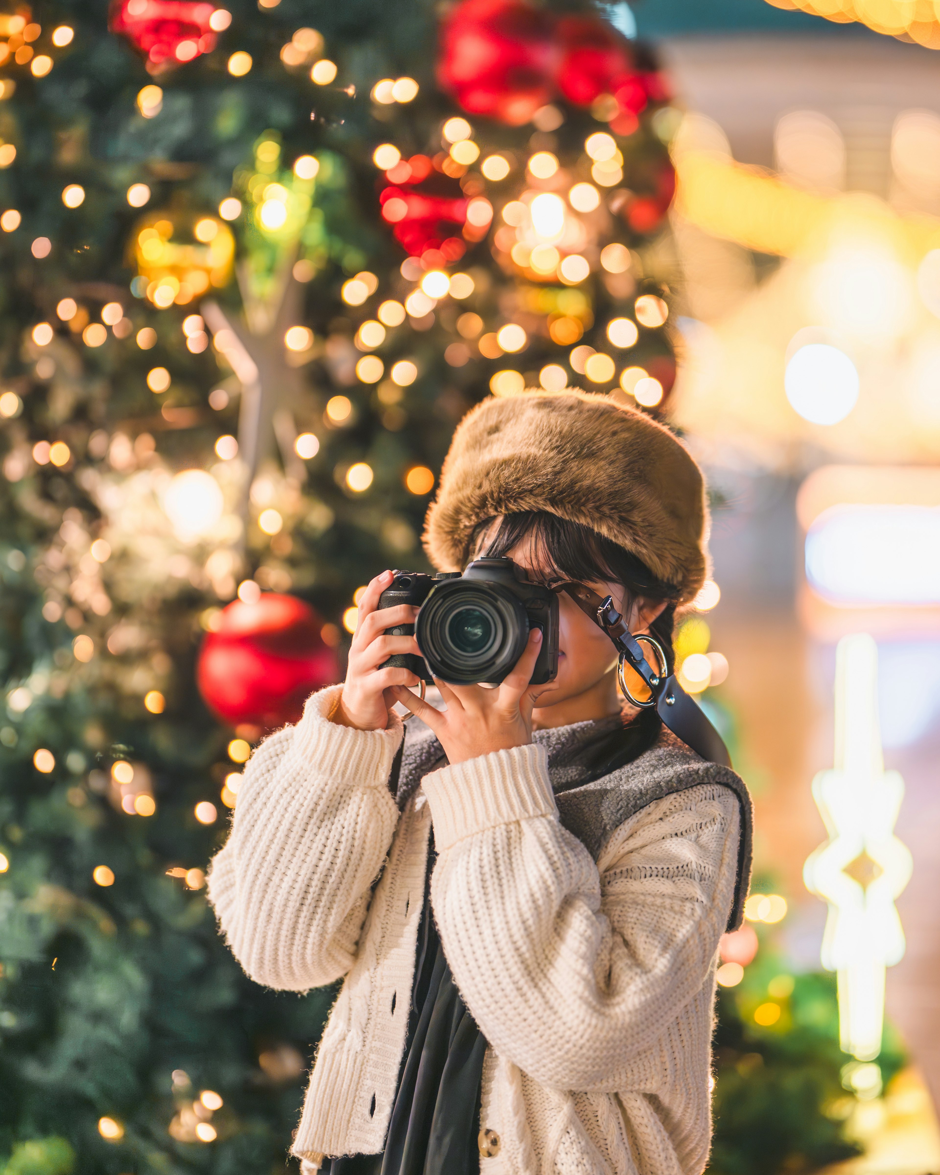 クリスマスツリーの前でカメラを持つ女性の写真