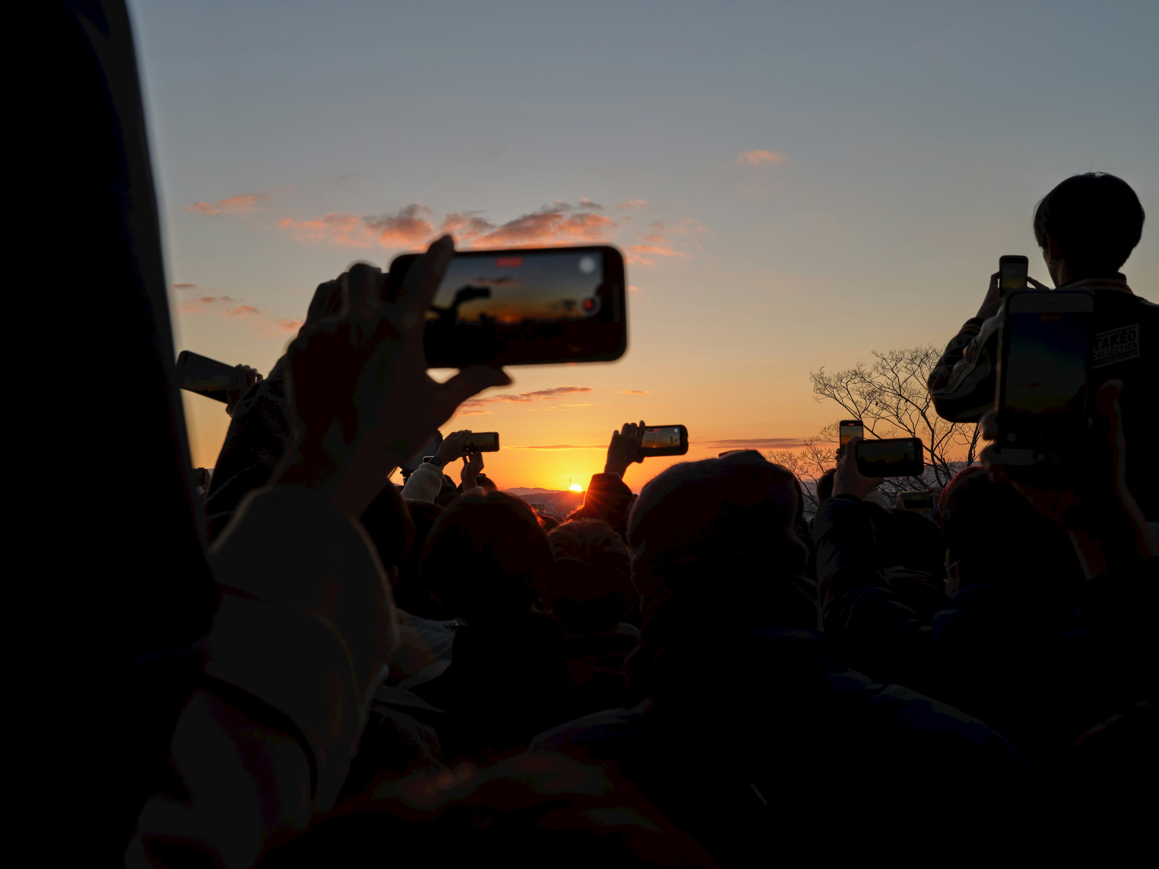 Silhouettes de personnes capturant le coucher de soleil avec des smartphones