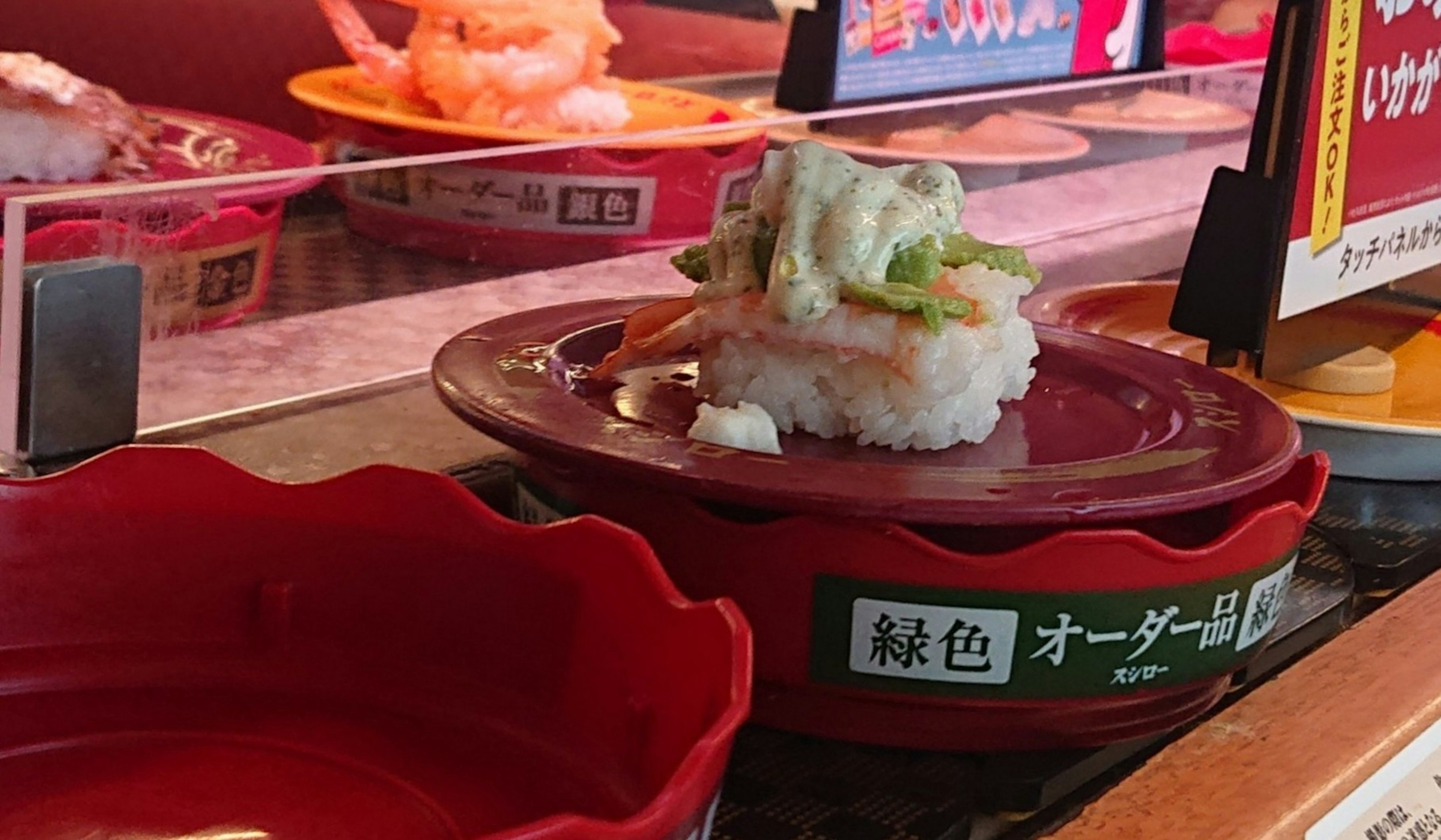 Un plato de sushi con cobertura verde en un plato rojo