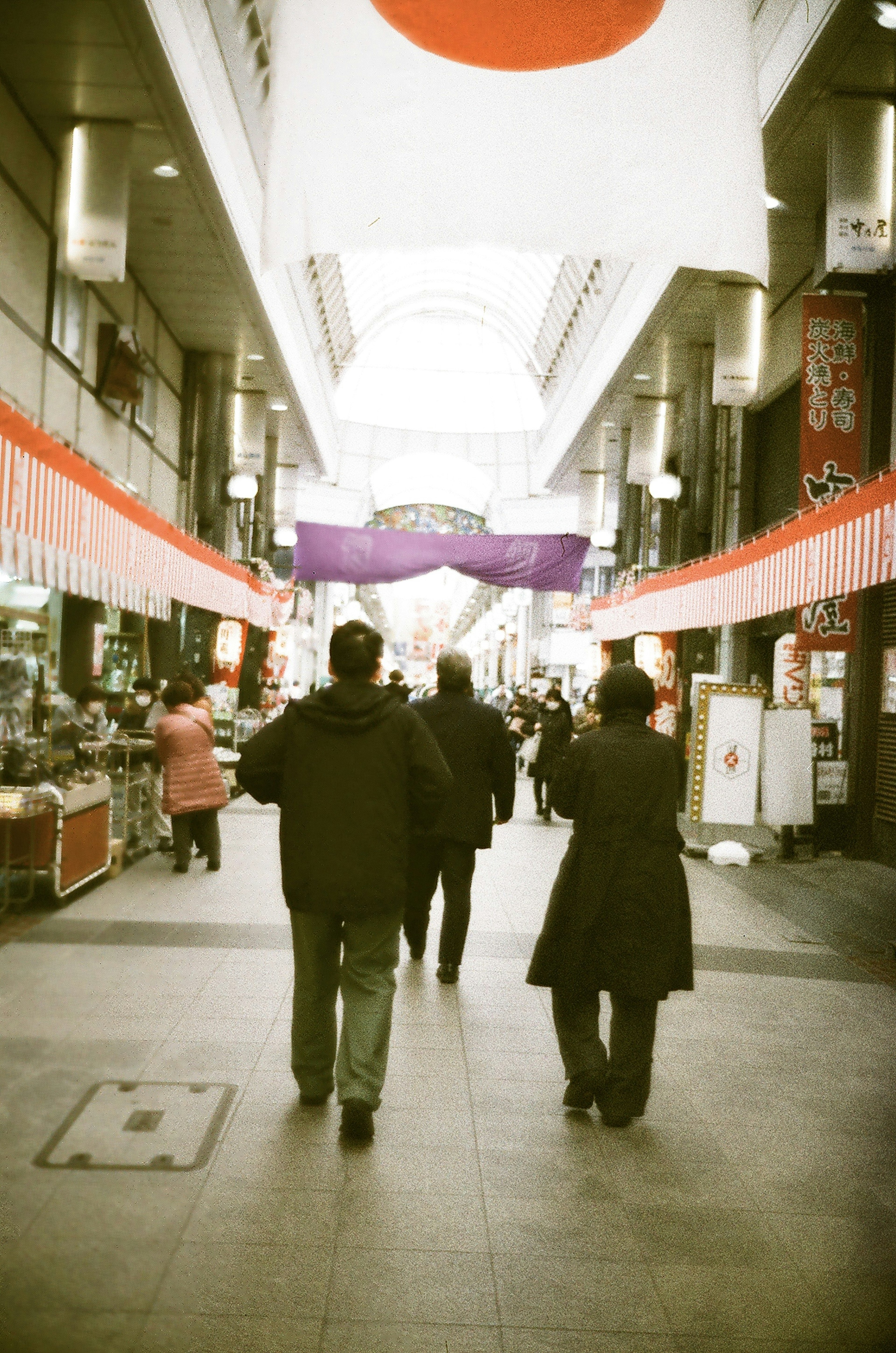 日本の商店街を歩く人々の後ろ姿と赤い日の丸の旗