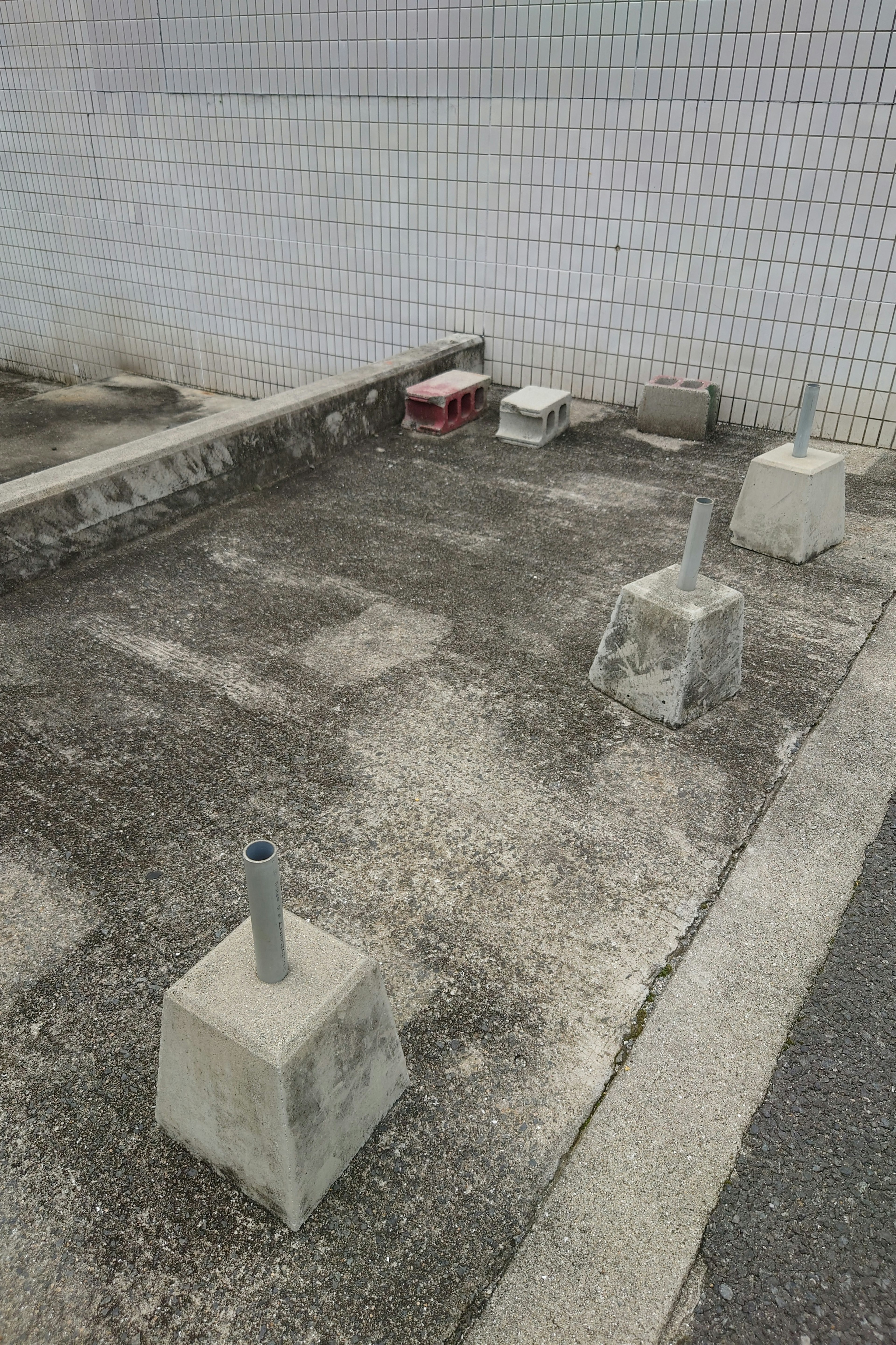 Image of a vacant lot with concrete foundations and a small red object near a wall