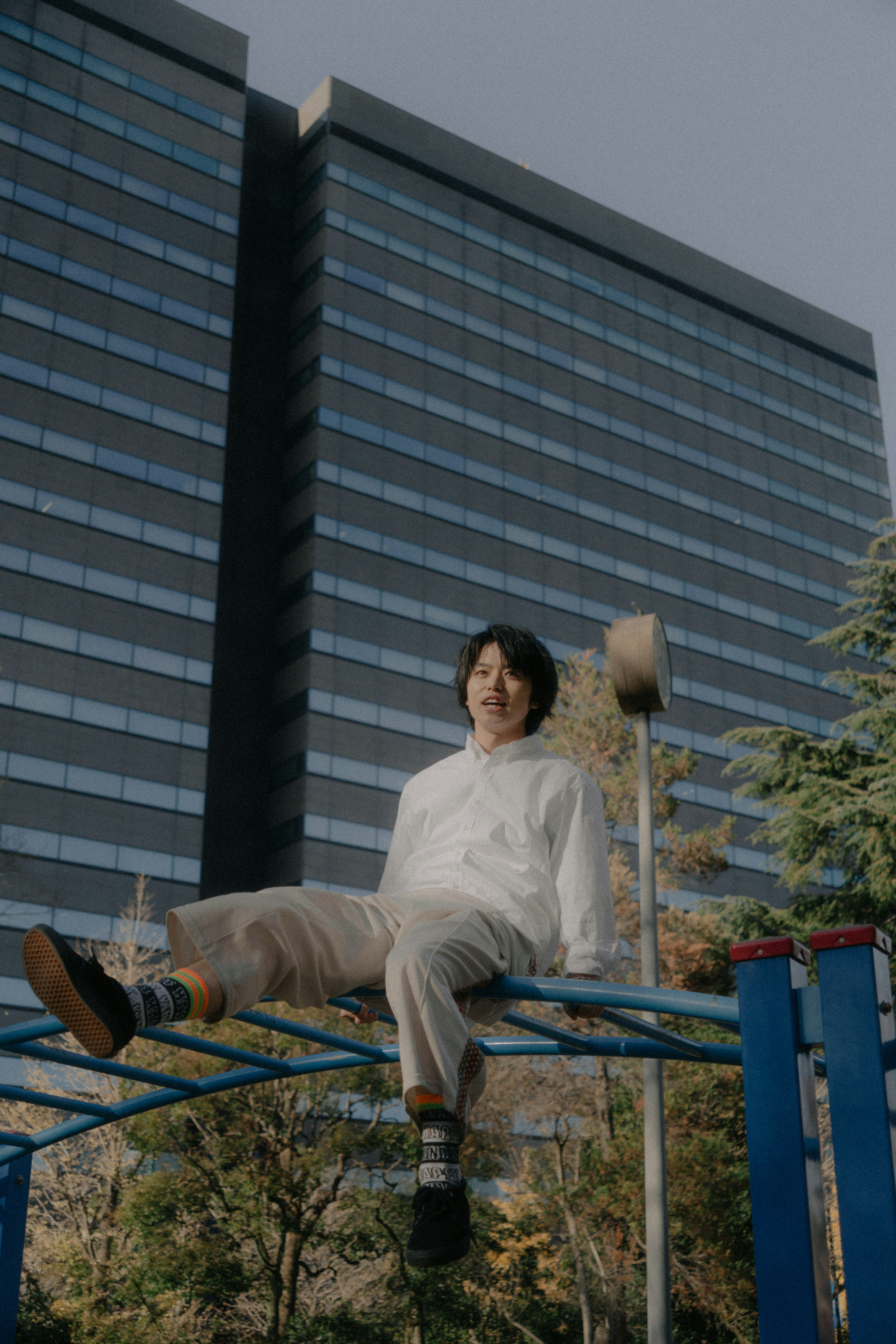 Hombre con camisa blanca y pantalones beige sentado en un equipo de juego frente a un edificio alto