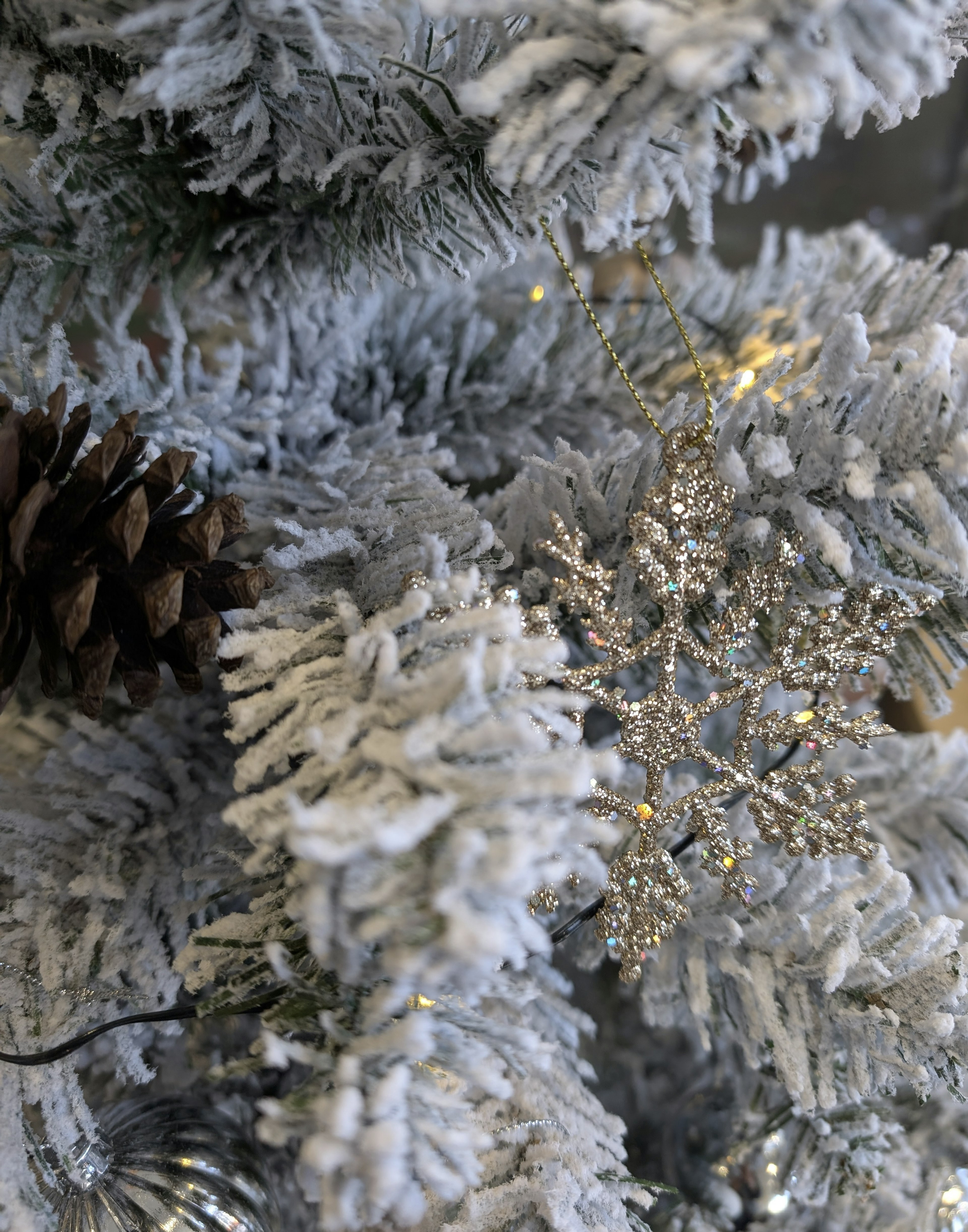 Gros plan sur un sapin de Noël blanc neigeux avec un flocon de neige argenté et un cône de pin