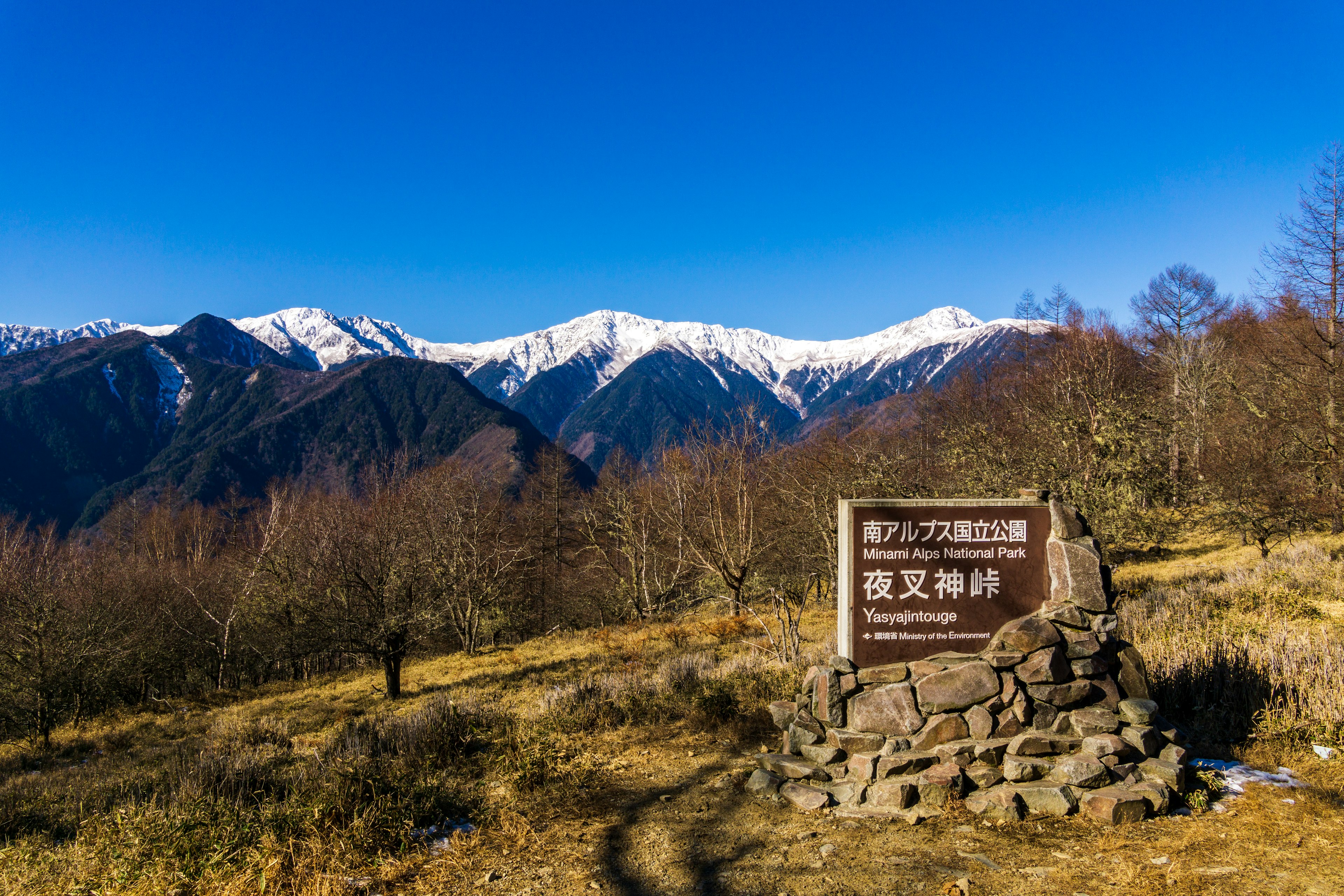 雪をかぶった山々と青空が広がる風景に立つ標識