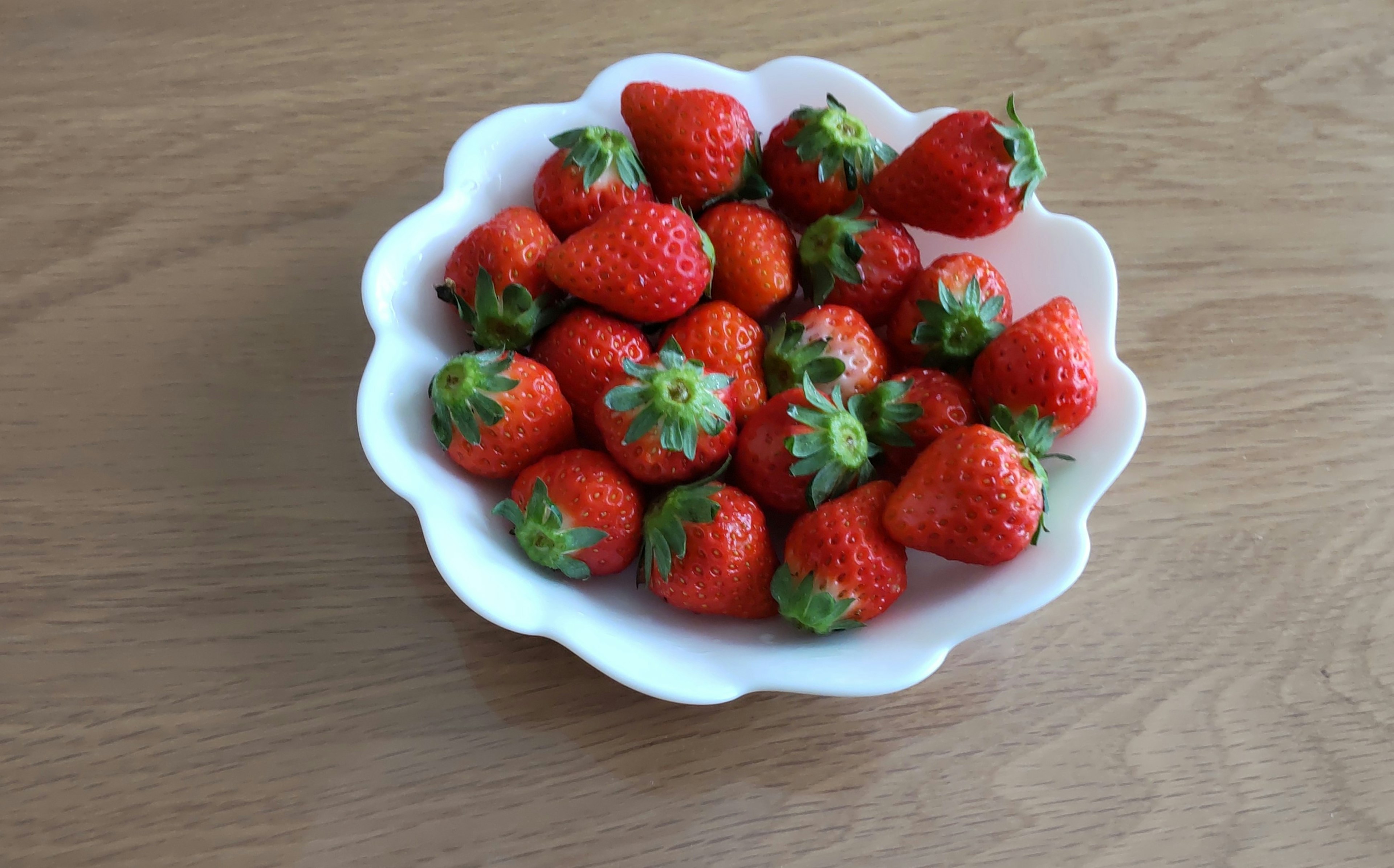 Fresh strawberries in a white bowl on a wooden table