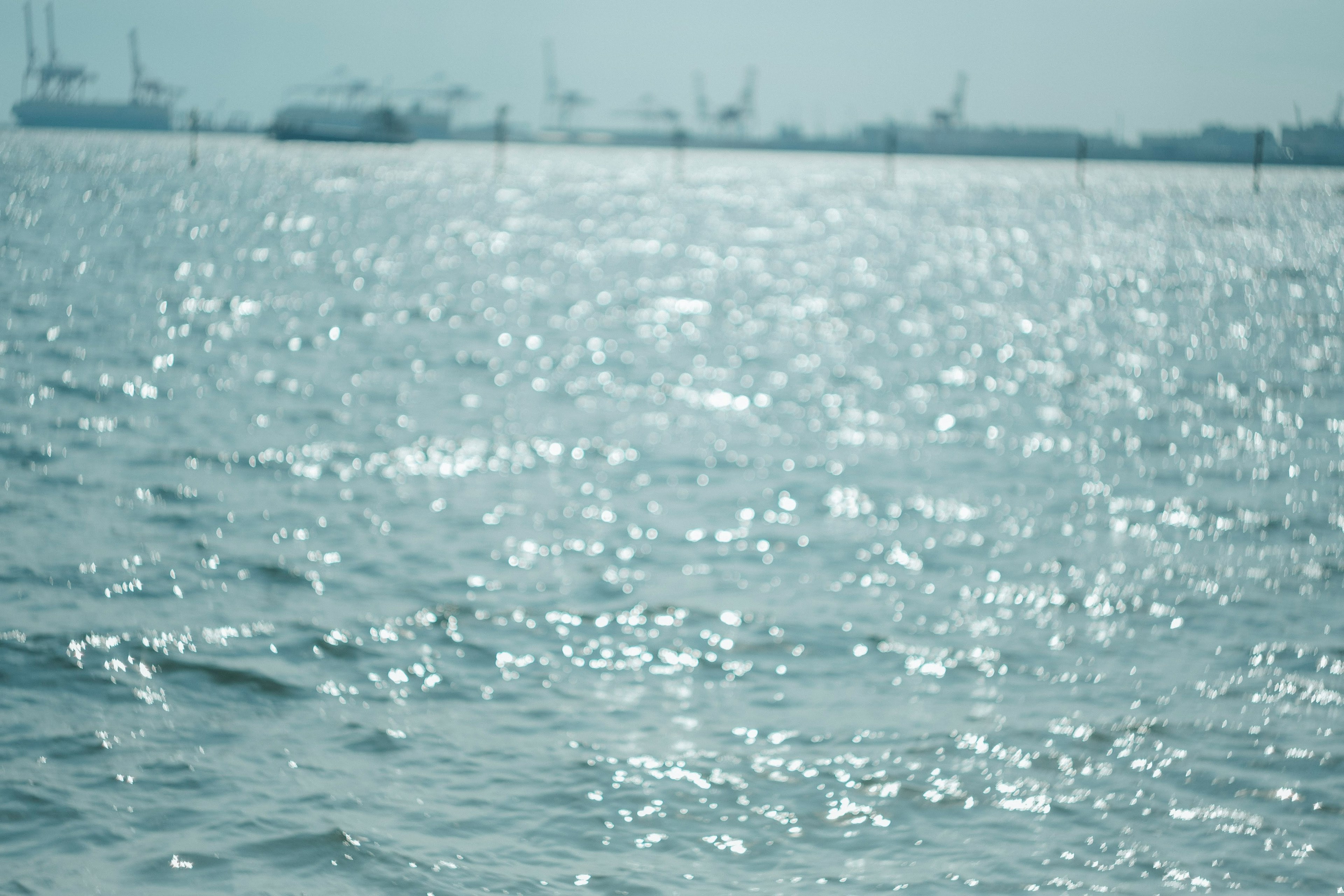 水面が光る海の風景と遠くに見える船やクレーン