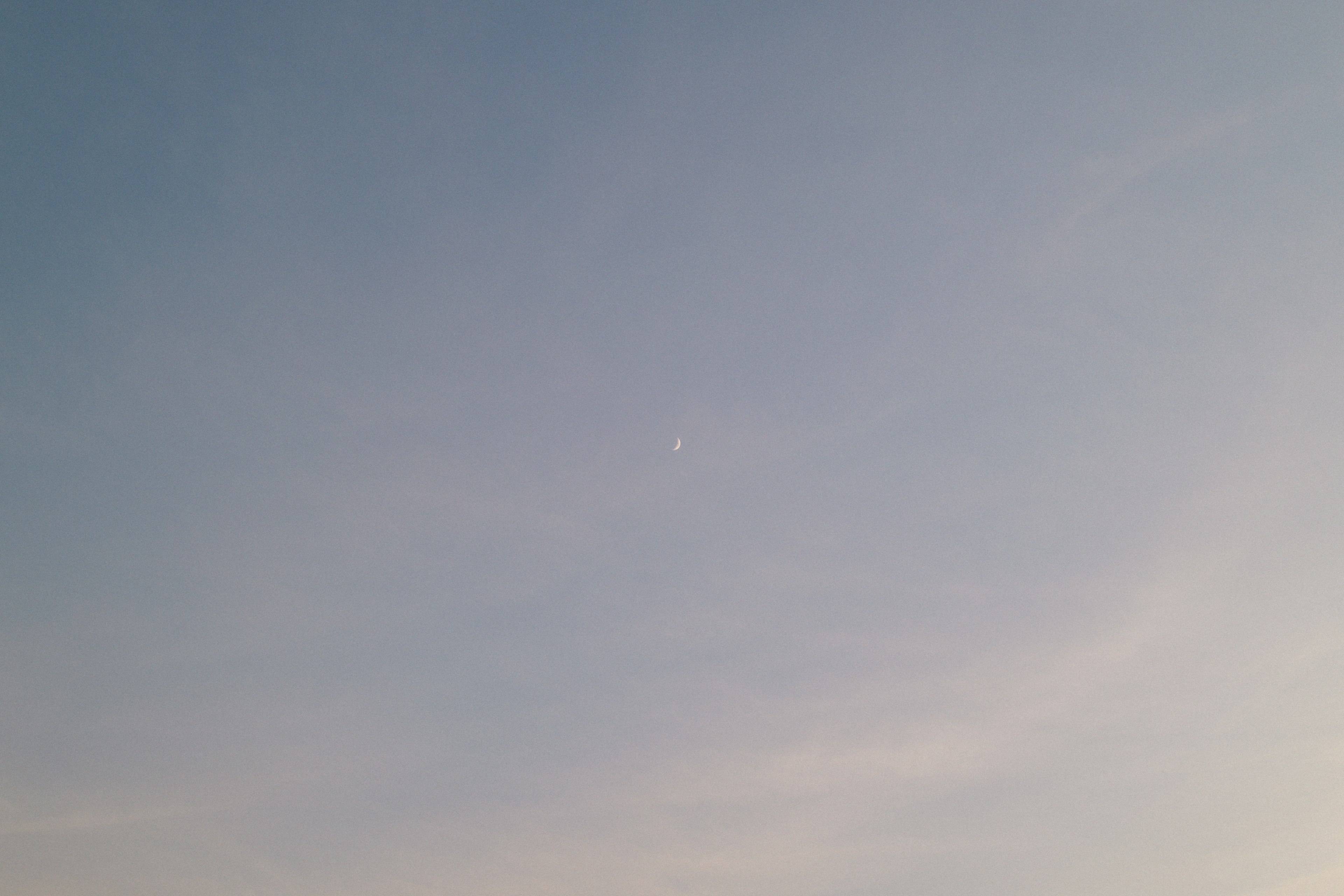 Una pequeña luna creciente visible en un cielo ligeramente nublado