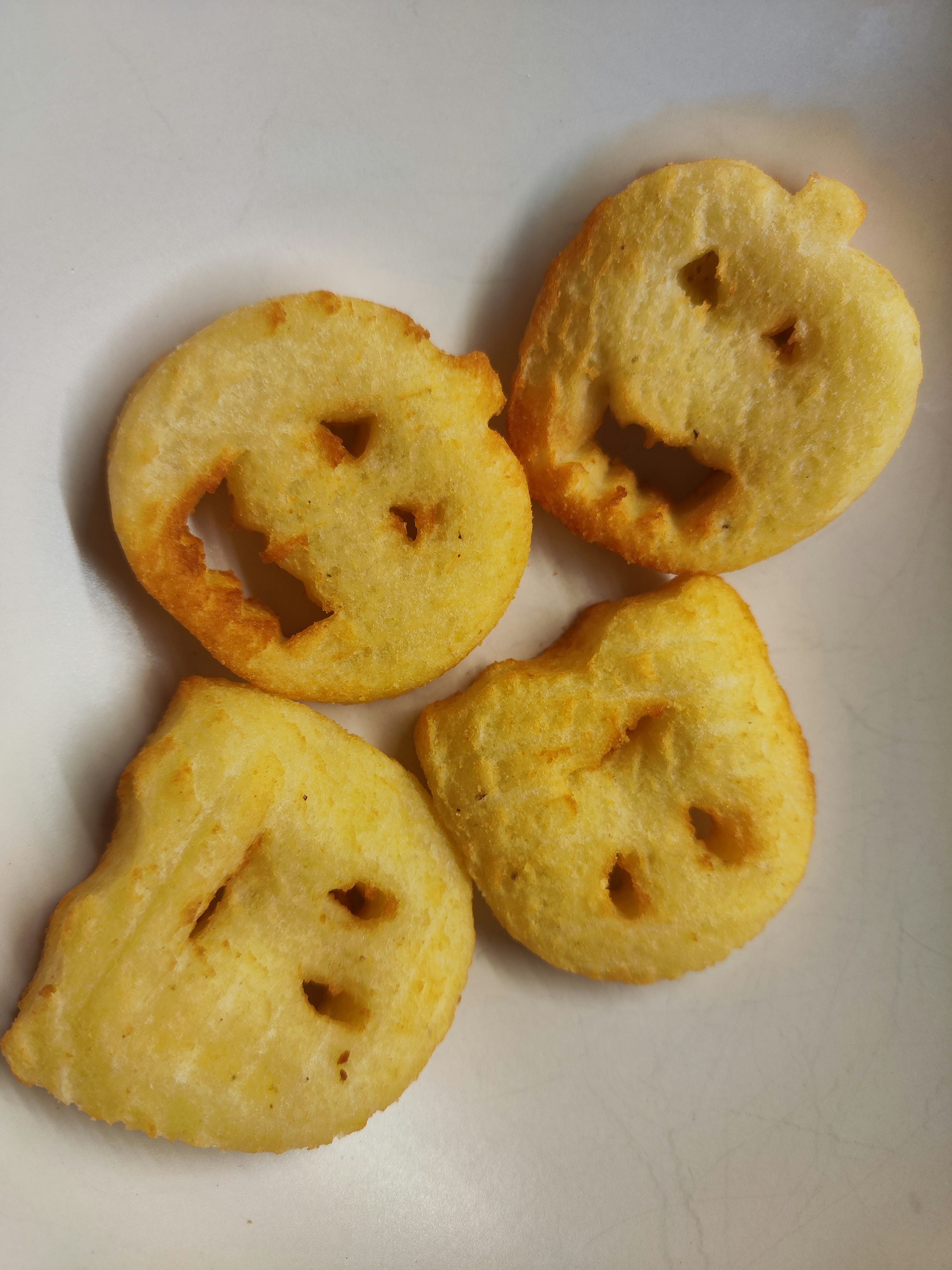 Four uniquely shaped fried snacks with faces arranged on a white plate