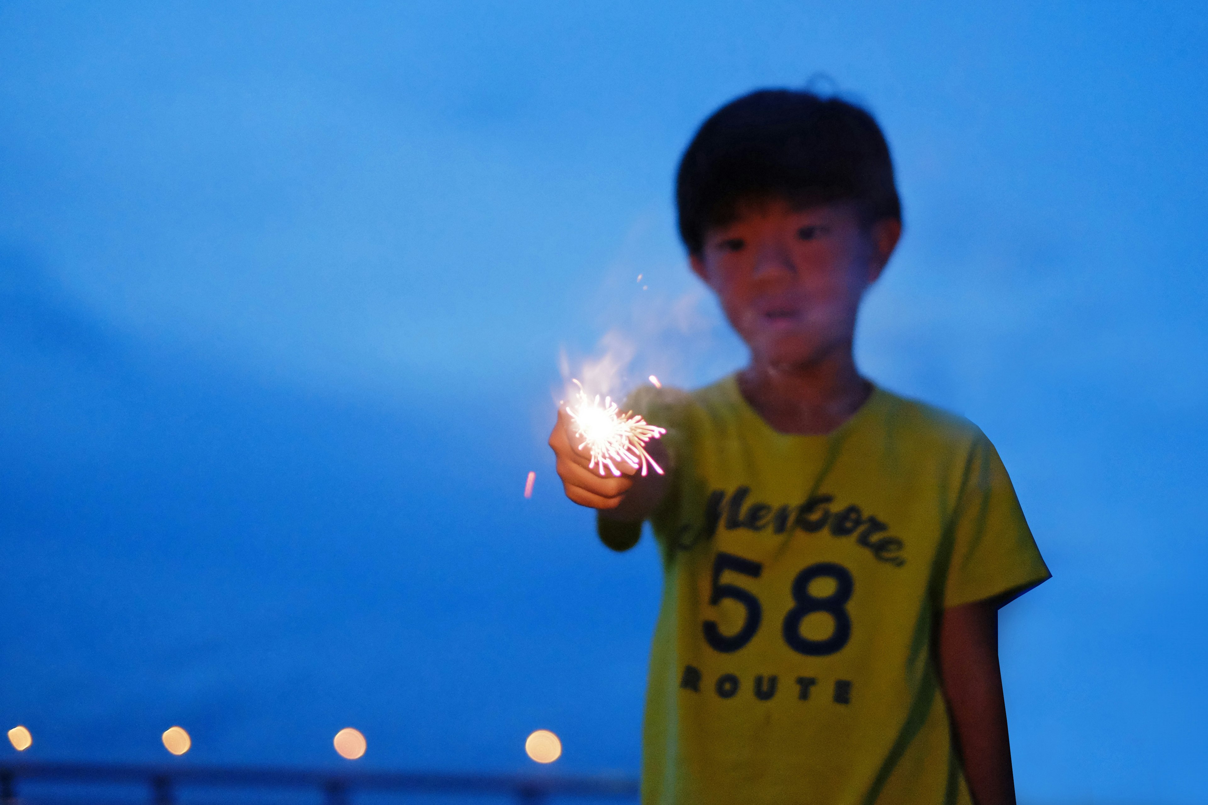 Niño sosteniendo un fuego artificial bajo un cielo azul