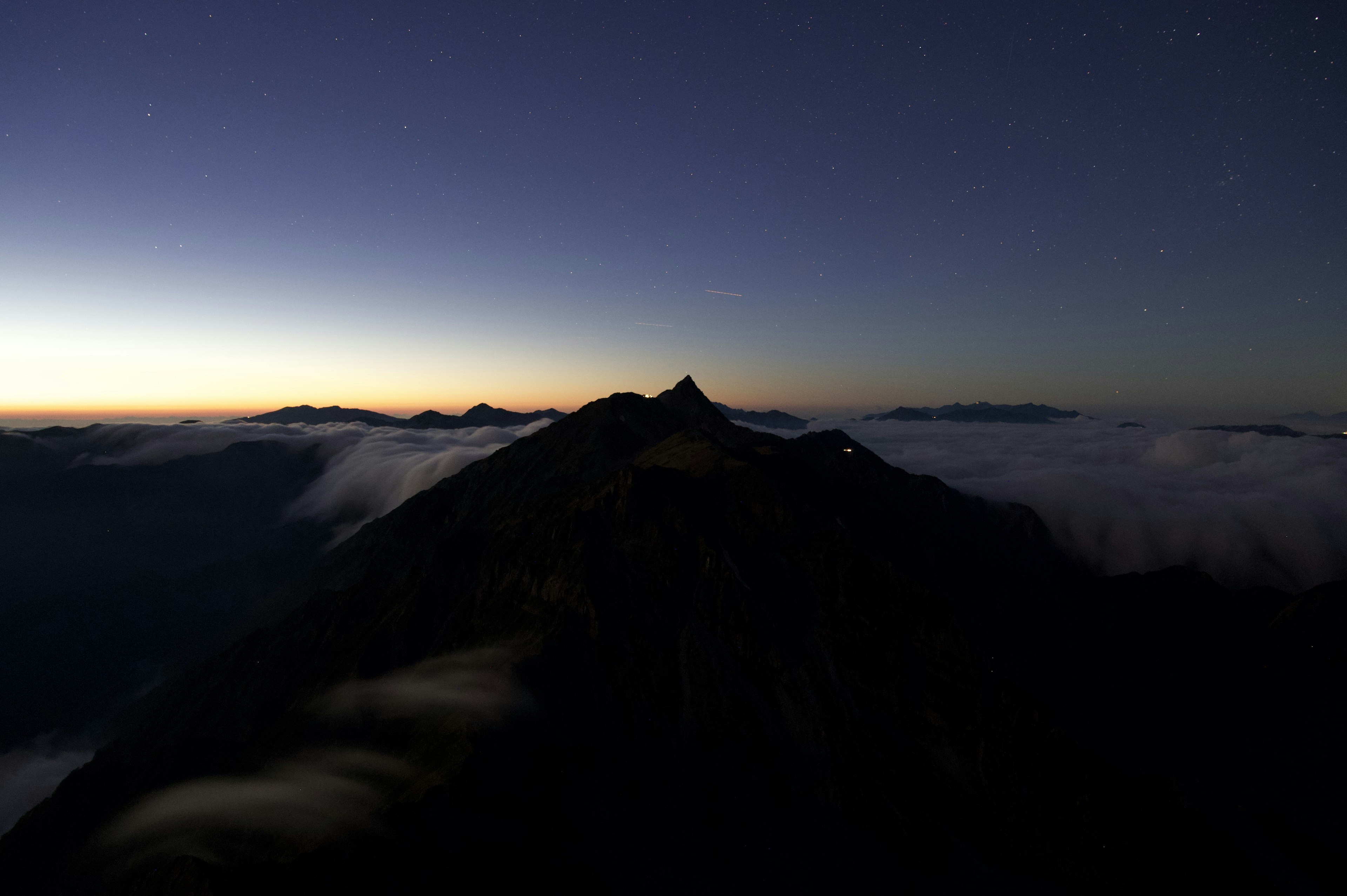 Silhouette of a mountain at dusk with a sea of clouds