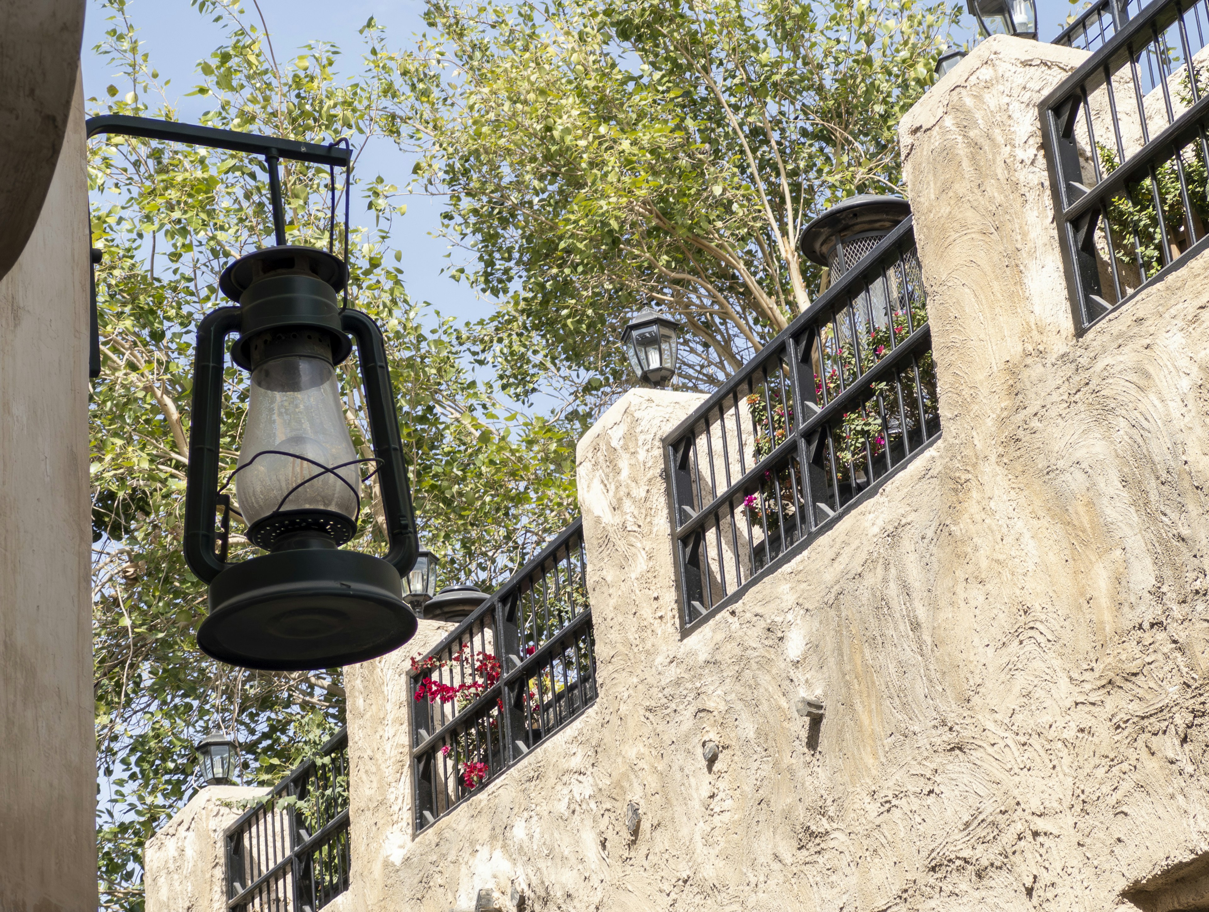 An old lantern hanging among trees with a stone wall backdrop