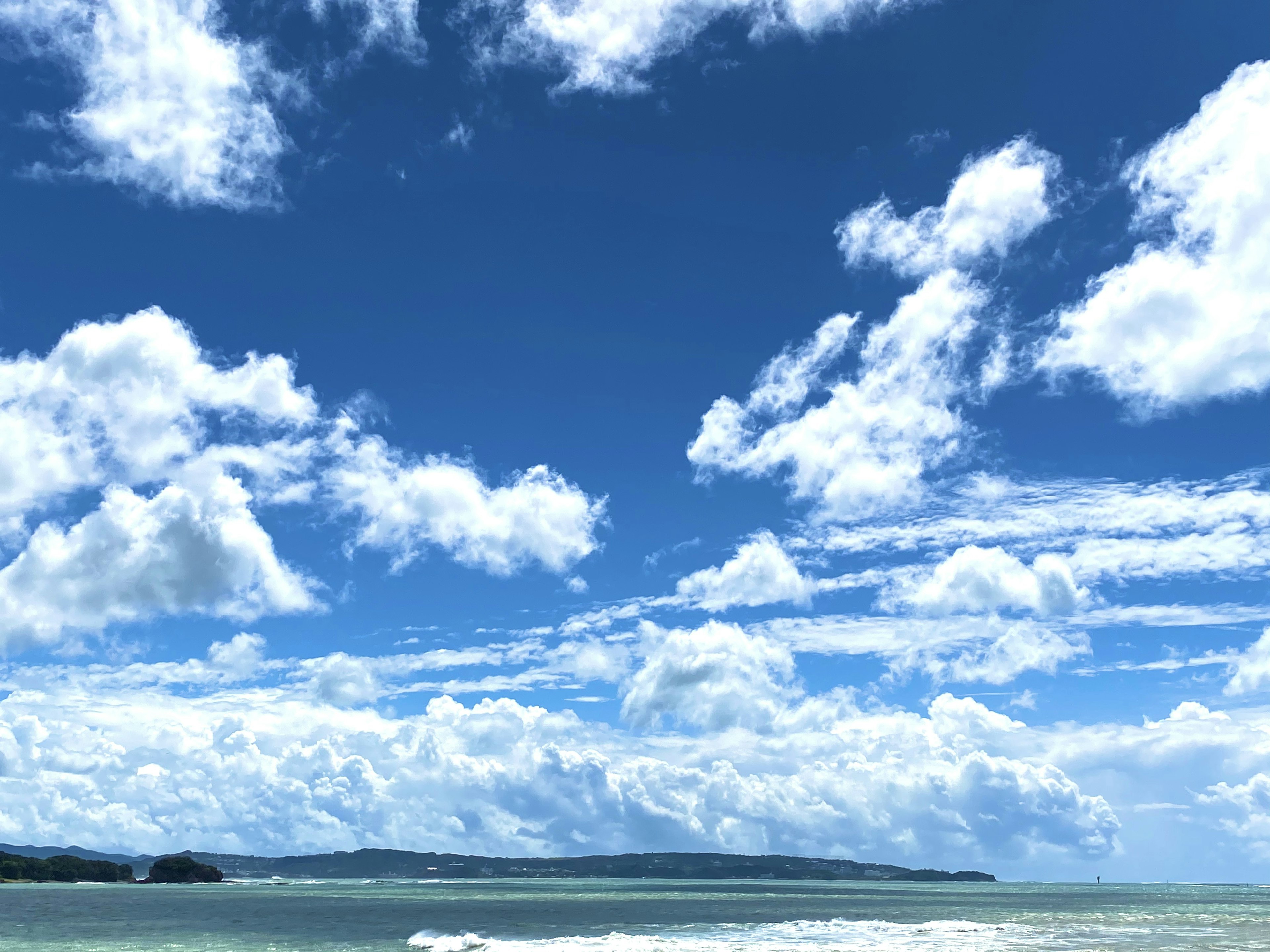 Pemandangan pesisir dengan langit biru dan awan putih berbulu