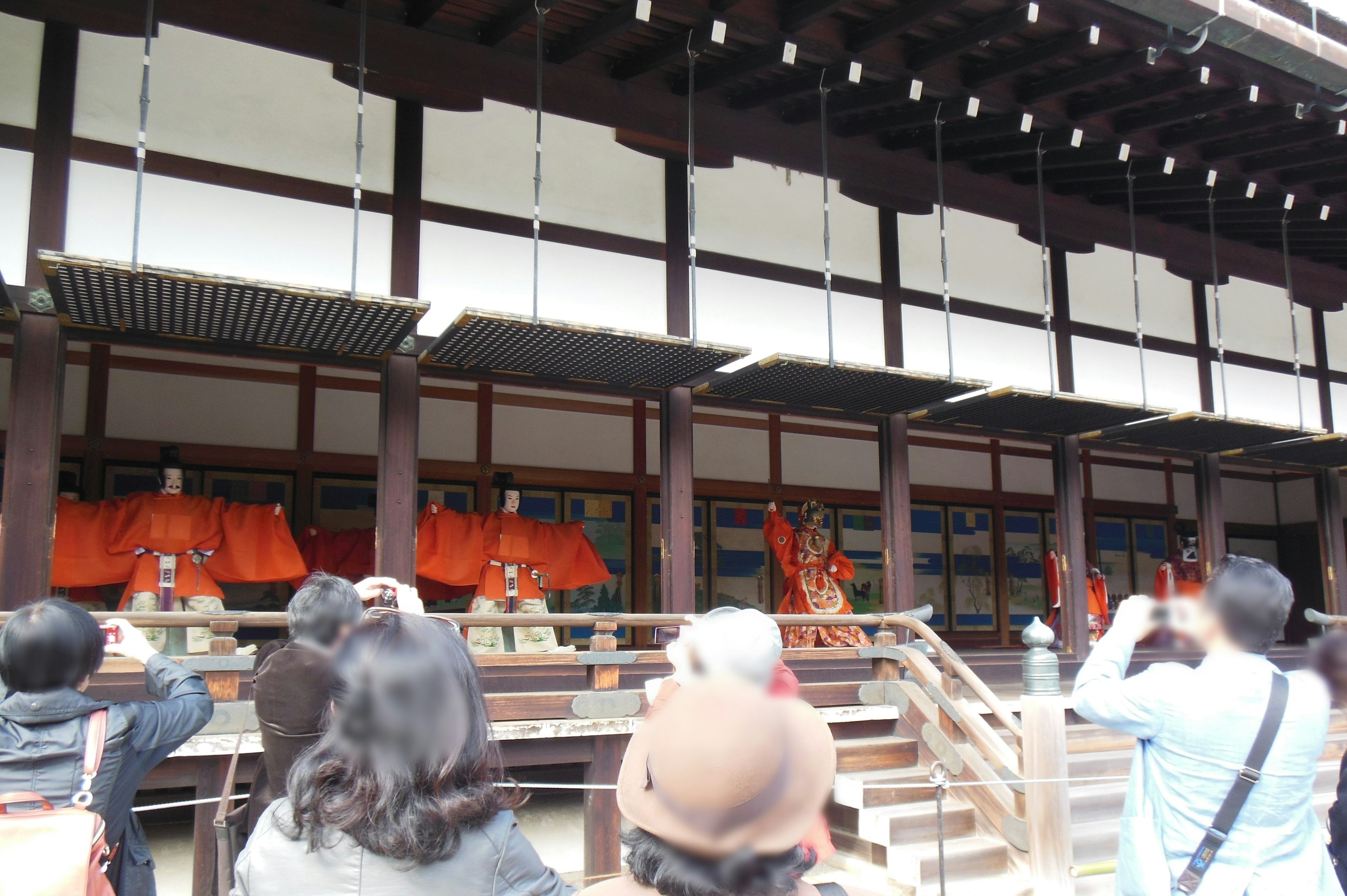 Visitantes tomando fotos de monjes en túnicas naranjas en un templo japonés