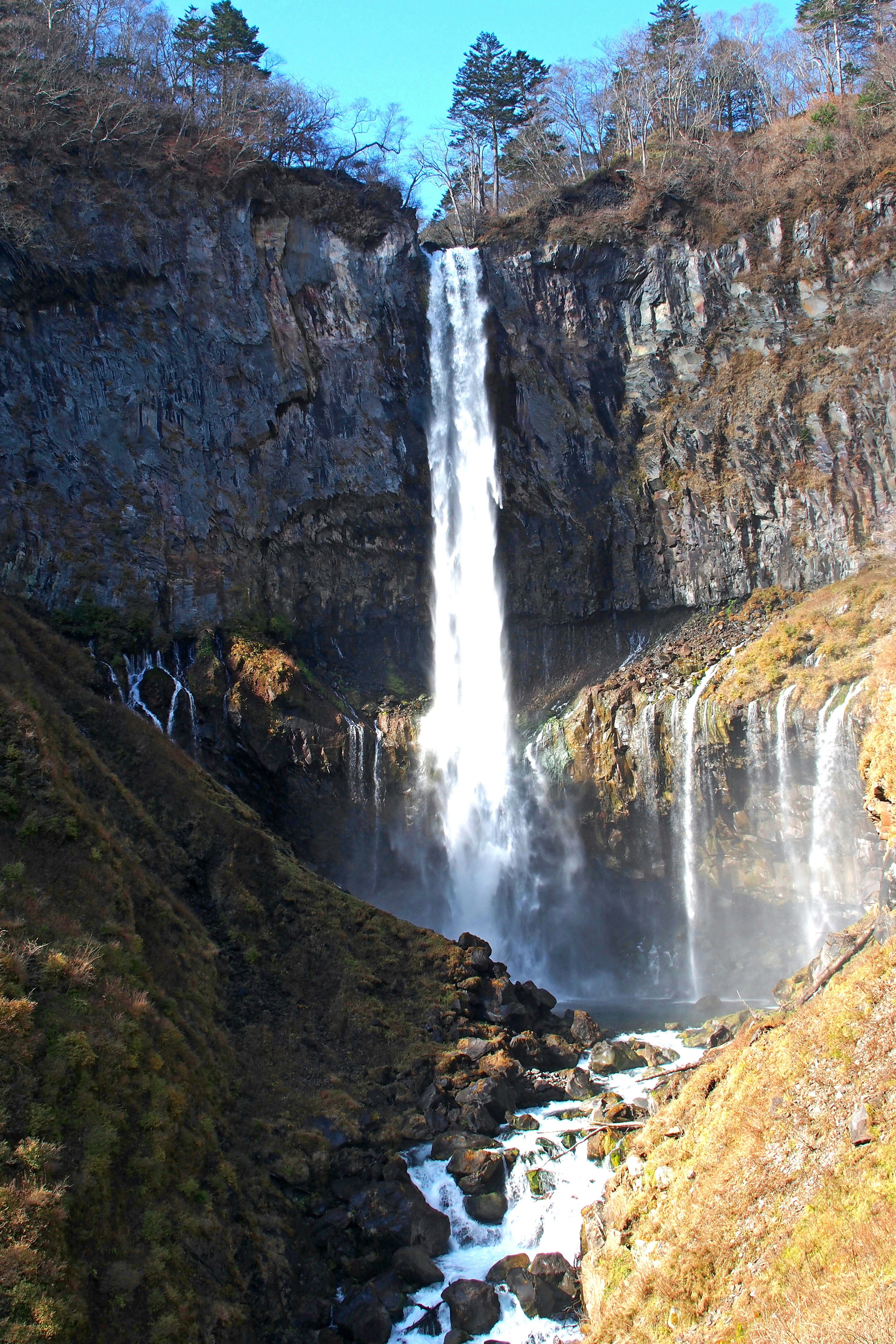 Impresionante cascada cayendo por acantilados rocosos con cielo azul claro