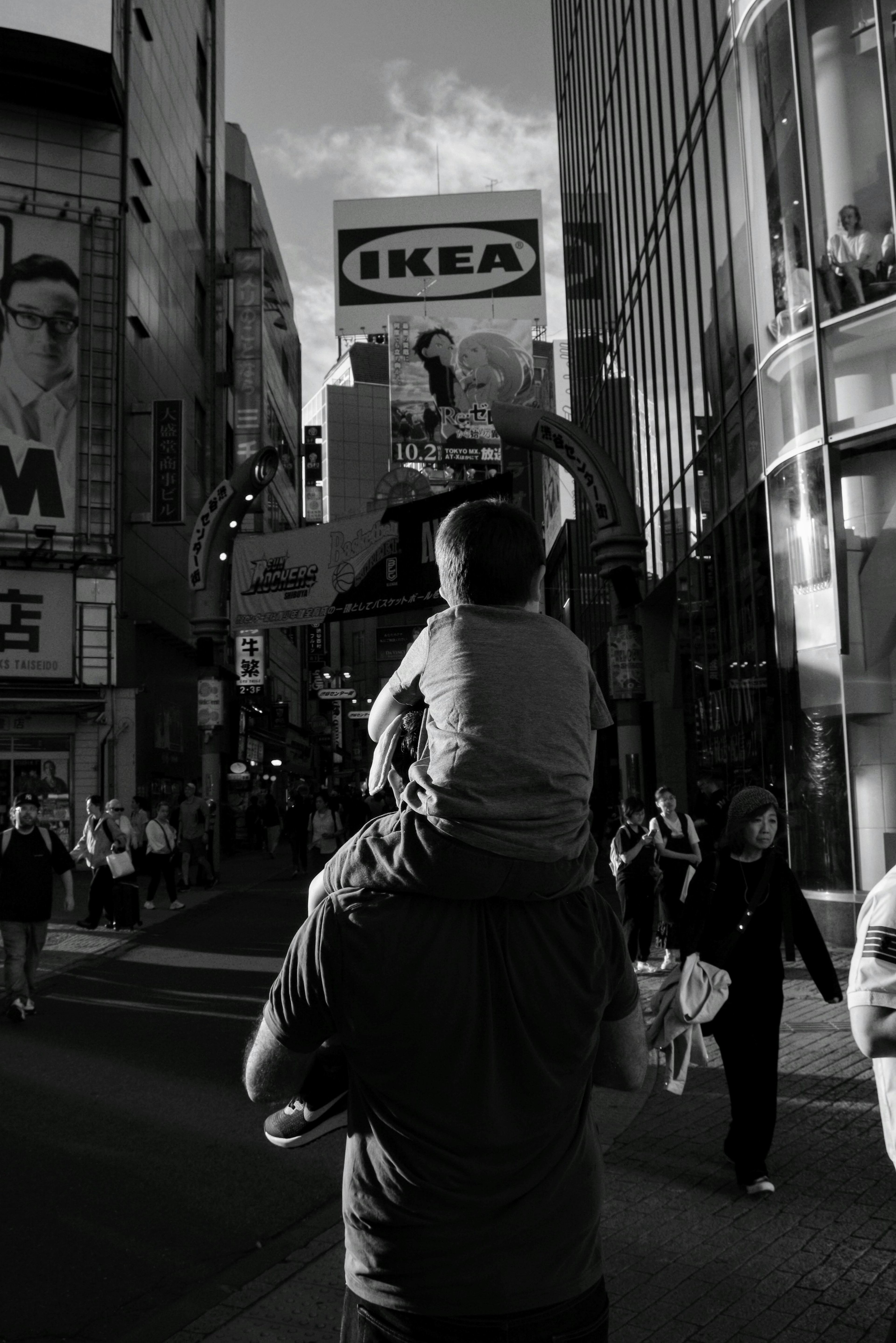 Un niño sobre los hombros de un padre mirando una calle bulliciosa en blanco y negro