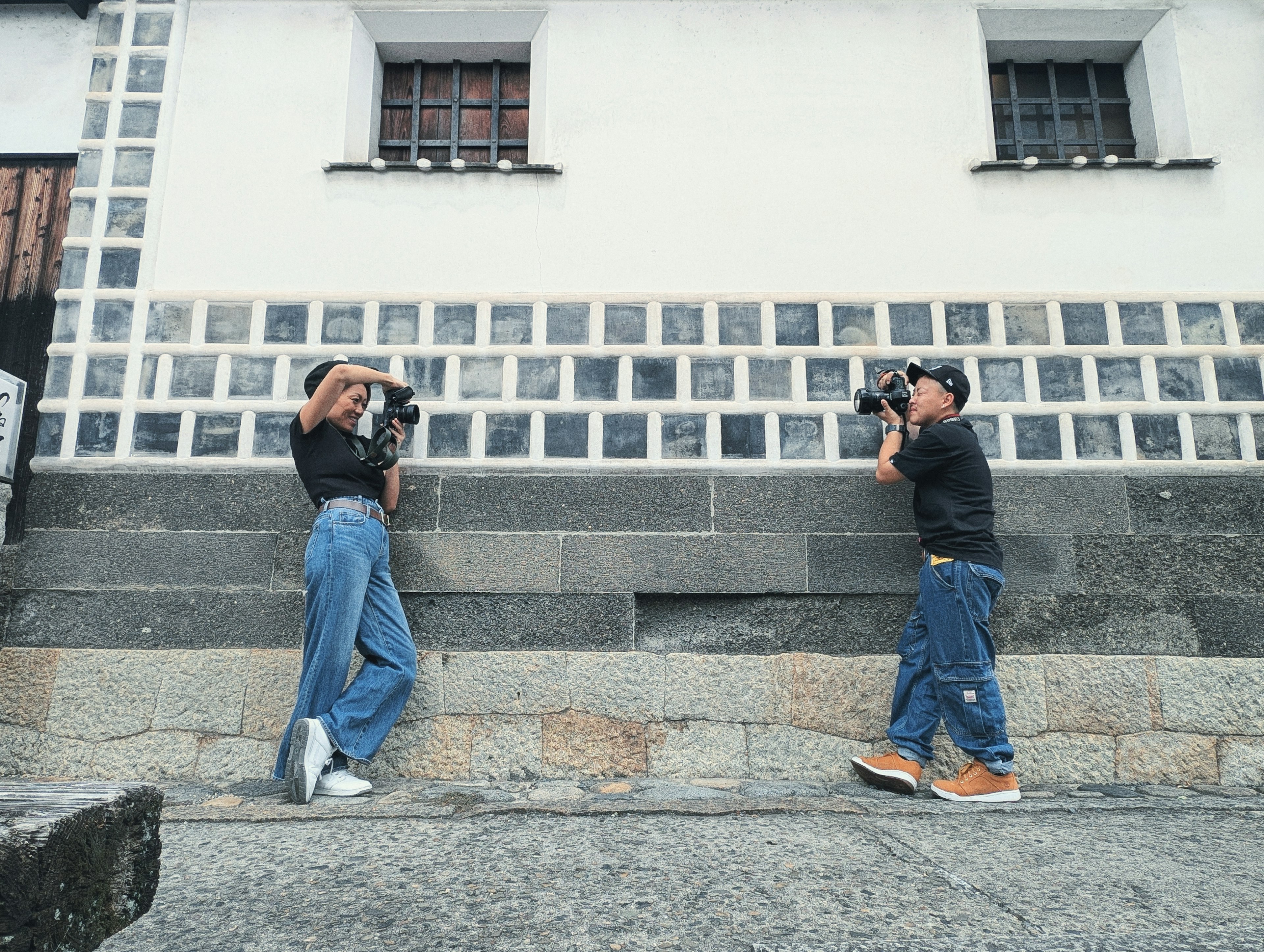 Due fotografi che si fotografano a vicenda davanti a un muro di pietra