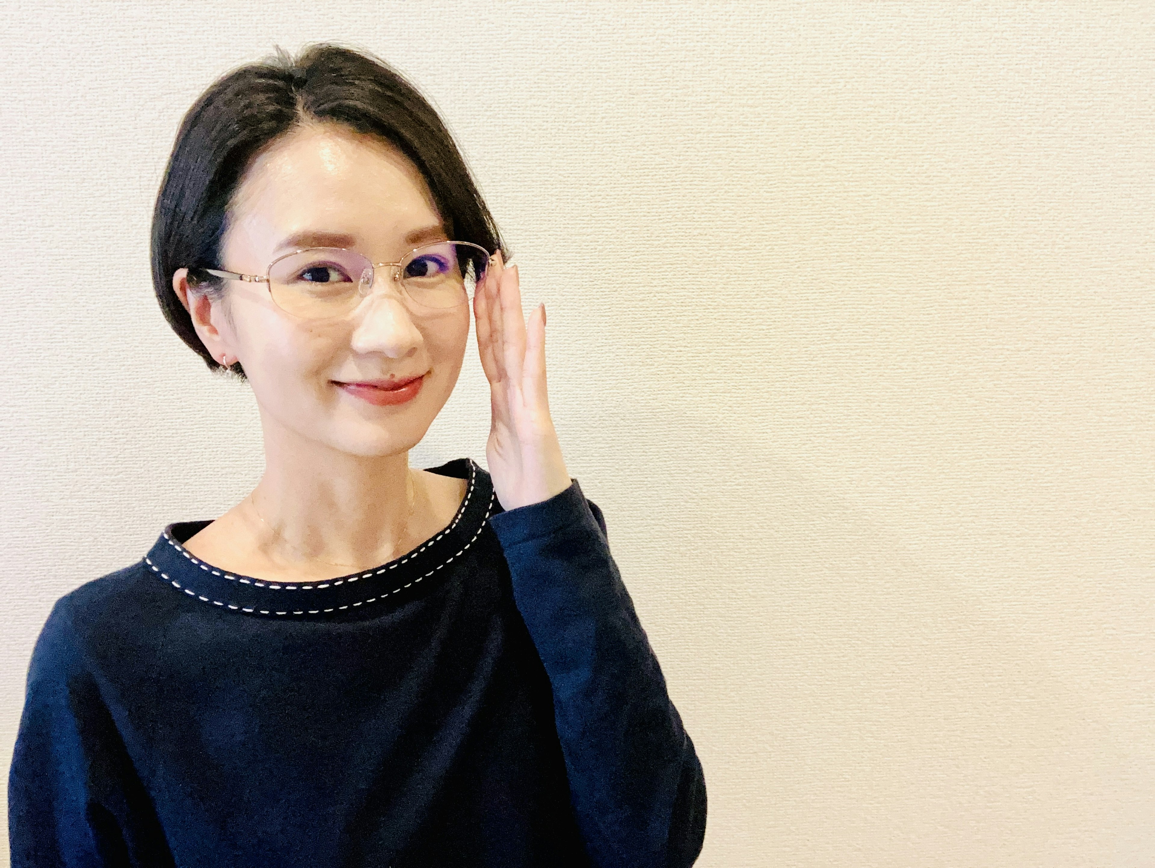 Une femme en pull noir ajustant ses lunettes et souriant