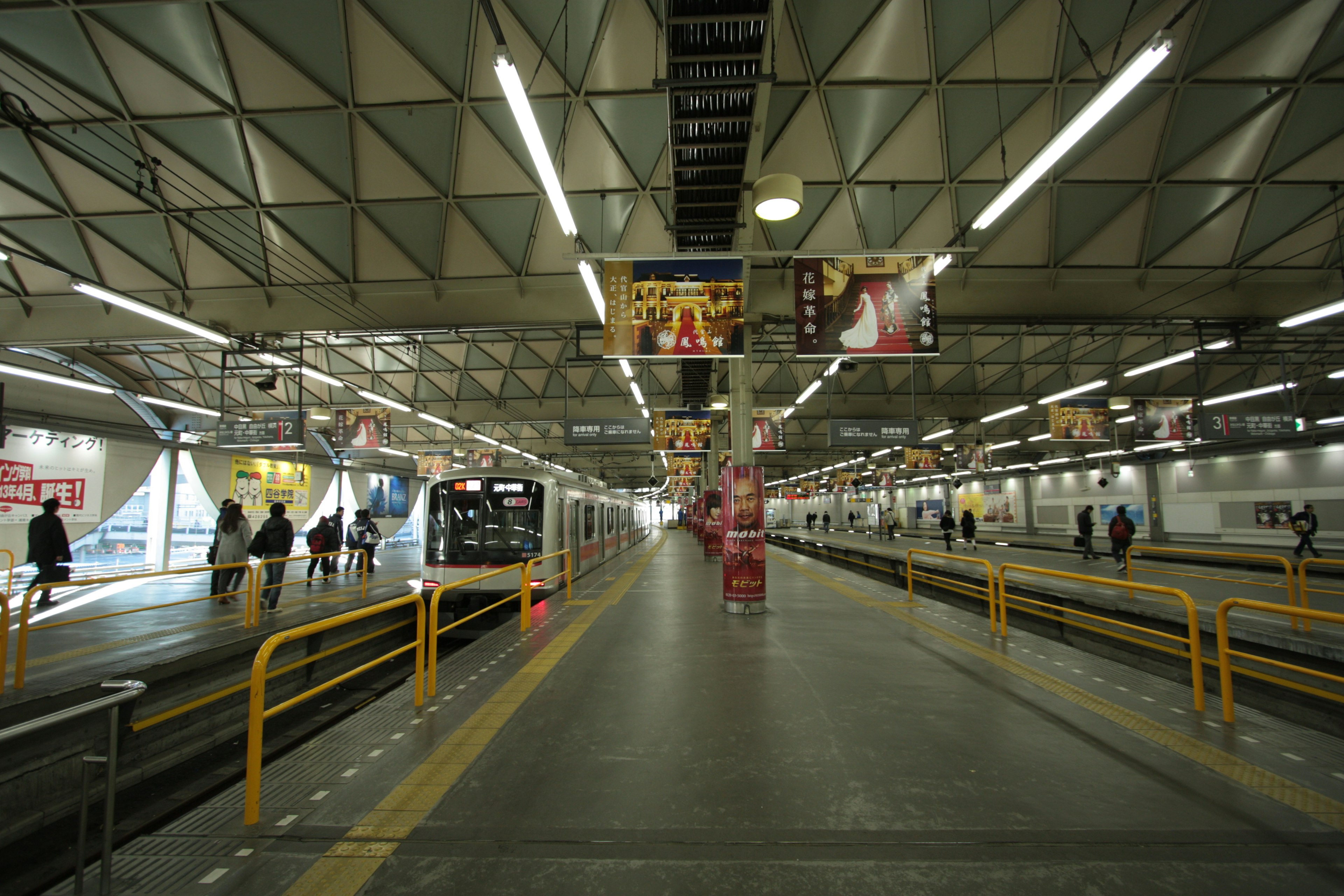 Personas caminando en una plataforma de tren con un techo triangular