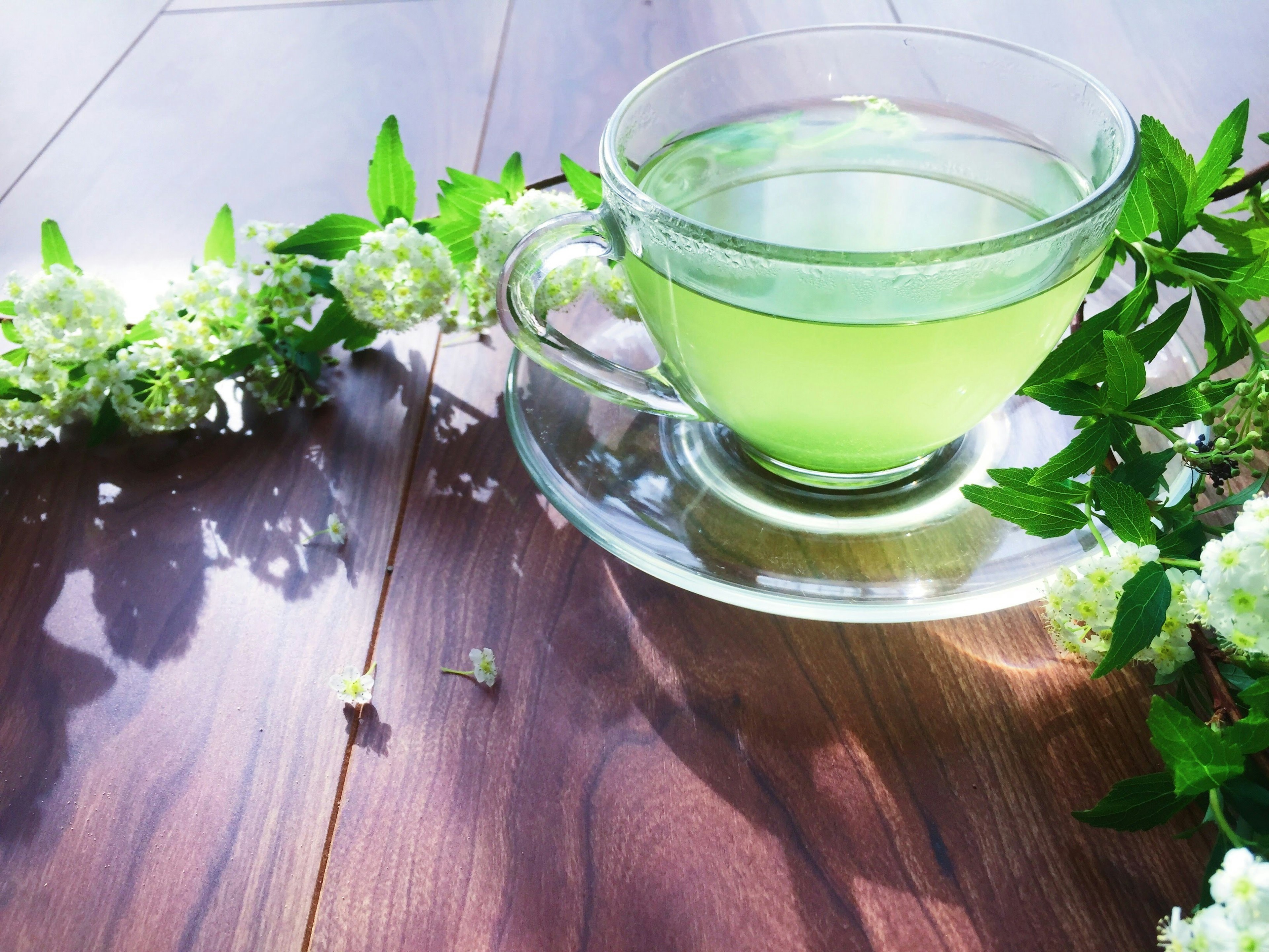 Taza de bebida verde rodeada de flores sobre una mesa de madera