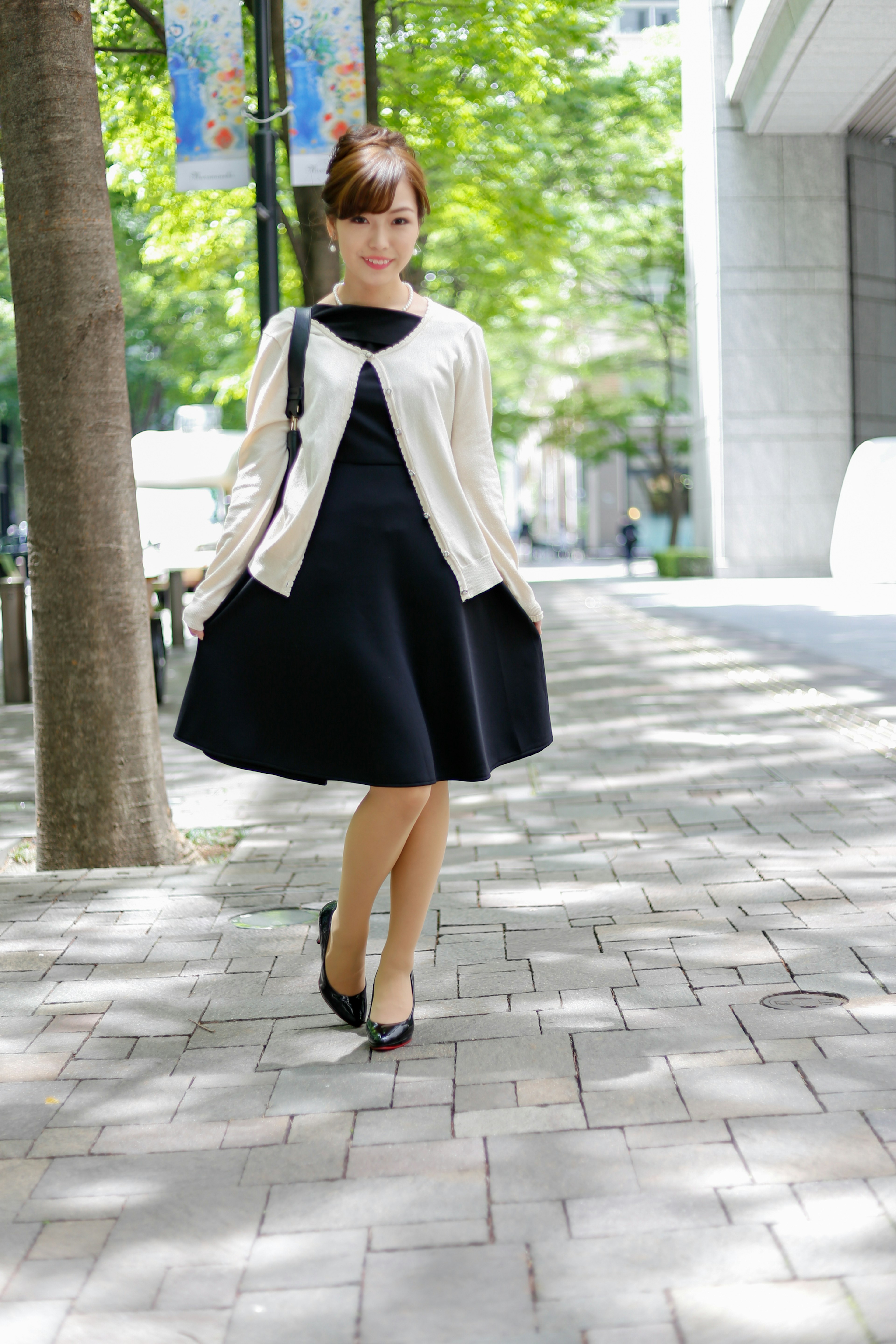 A woman wearing a black dress and white cardigan walking on a city street