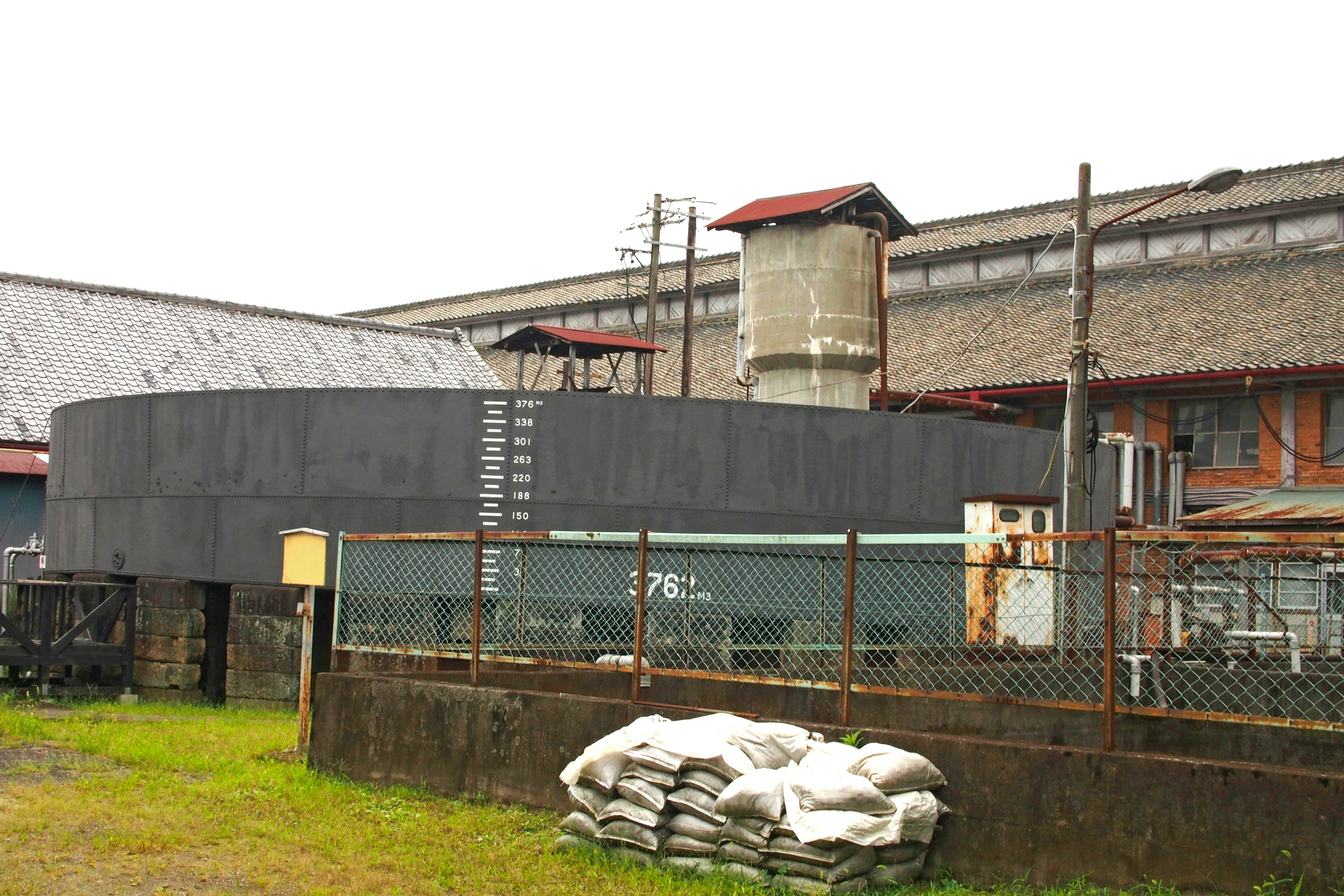 A view of an industrial area featuring a circular structure and an older building in the background