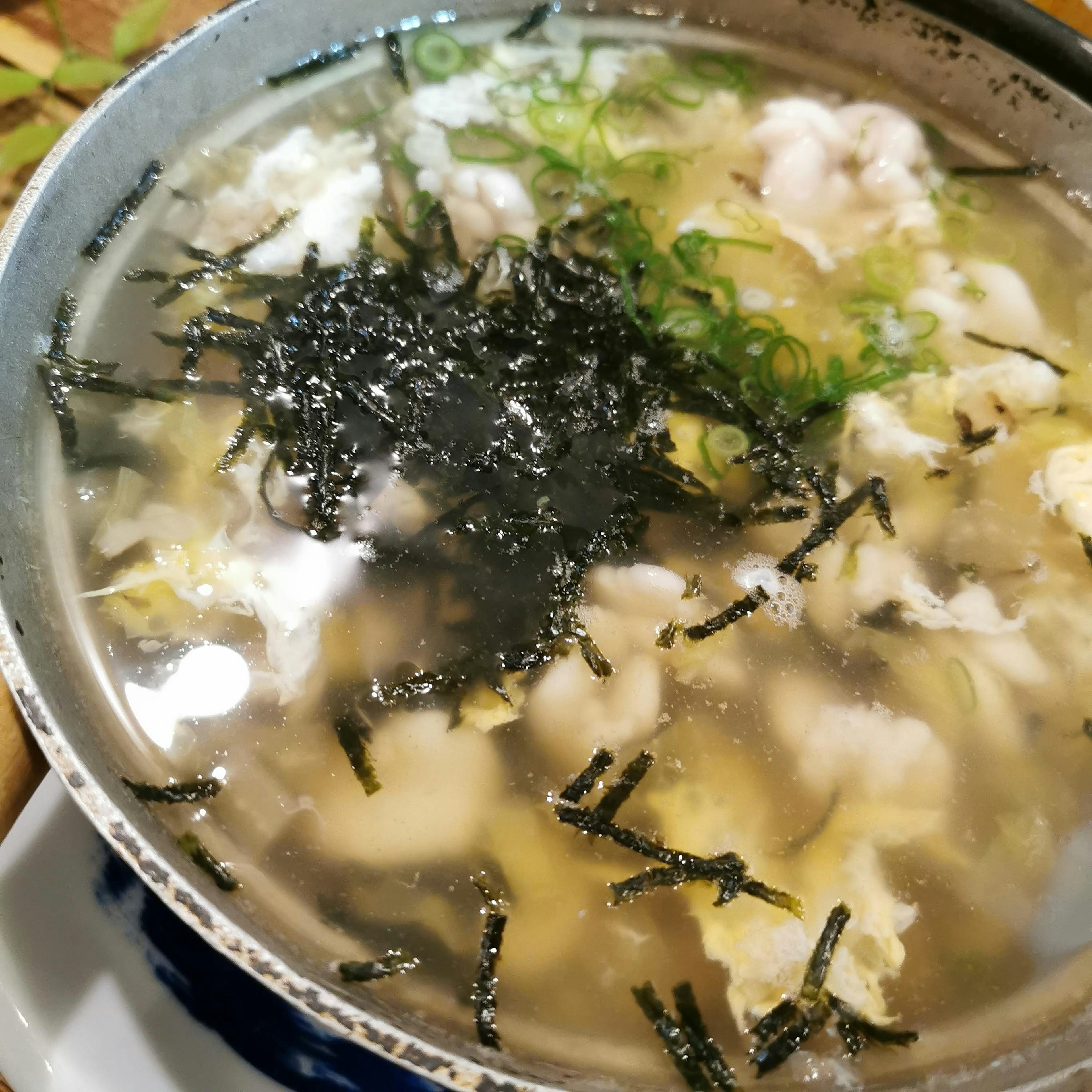 A bowl of clear soup with green onions and seaweed floating on top