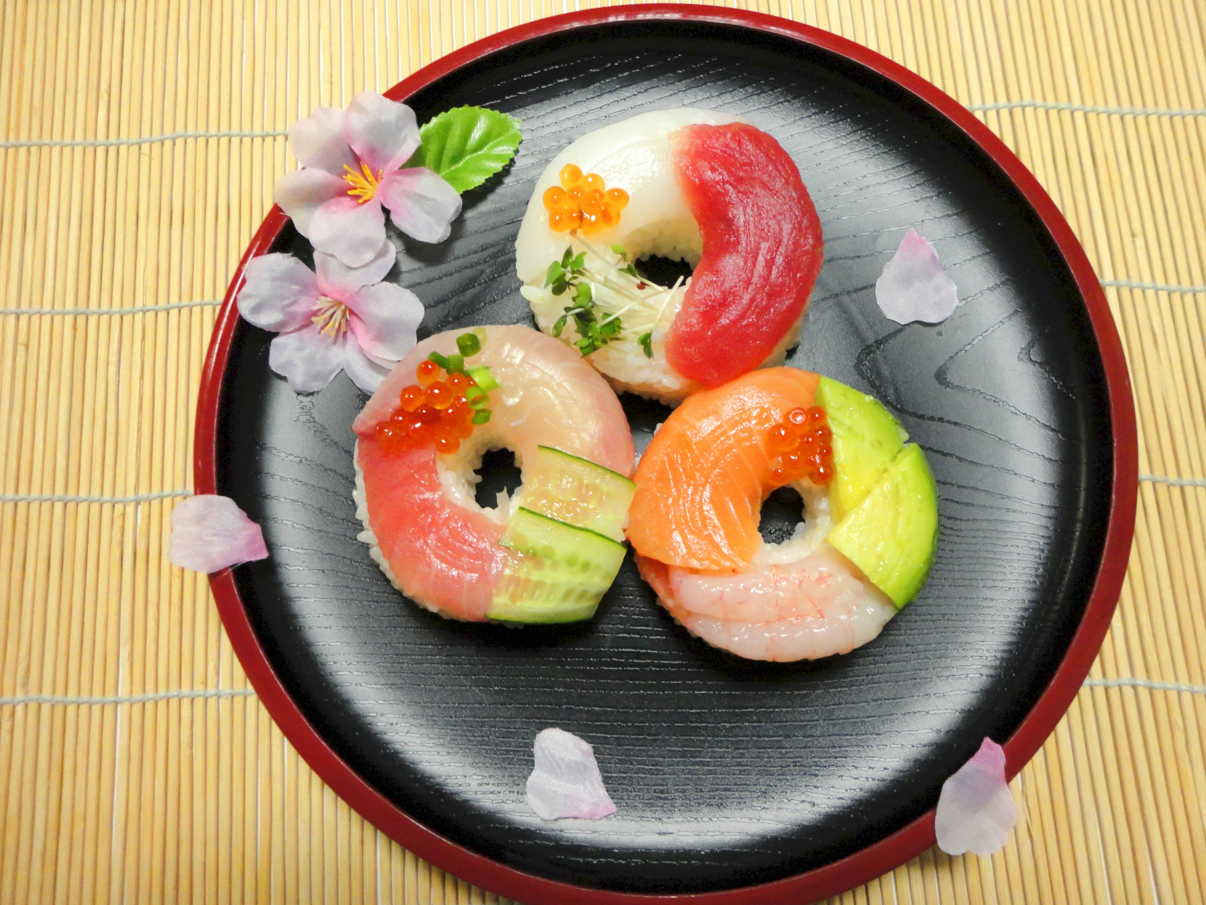 Colorful sushi donuts arranged on a black plate with floral decorations