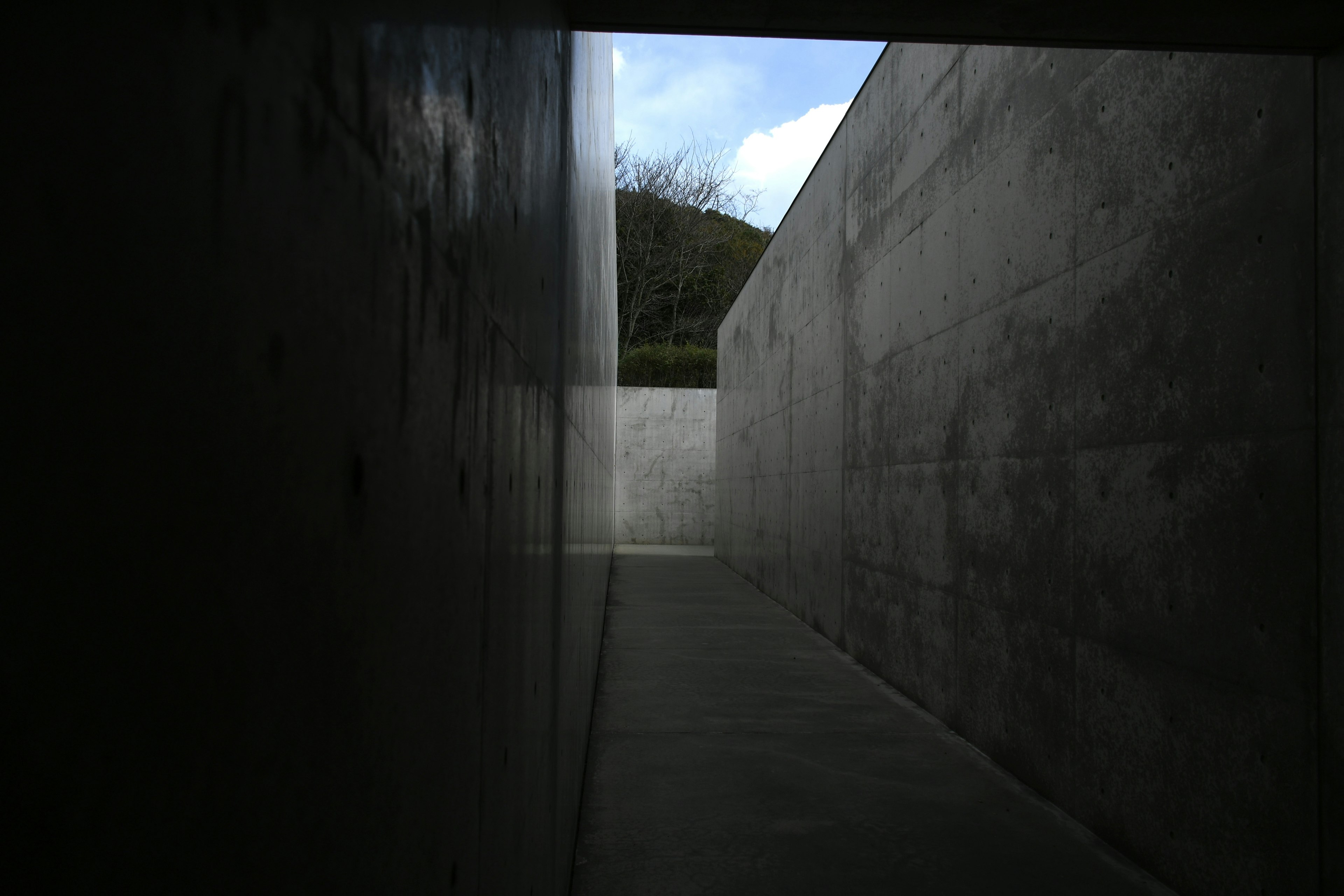 Narrow concrete passageway leading to a blue sky